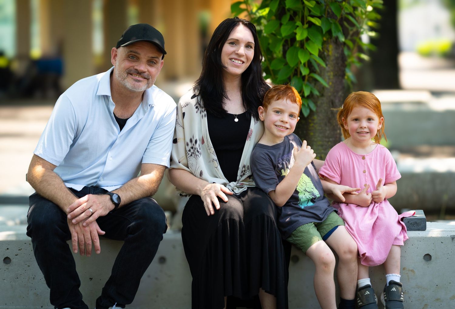 A family sits outdoors together on a concrete ledge chatting and bonding in casual clothing.