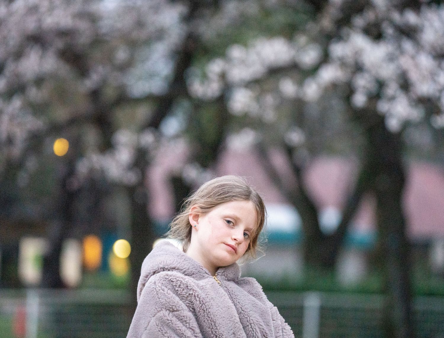 Portrait in a fluffy gray hoodie against blurred cherry blossoms.