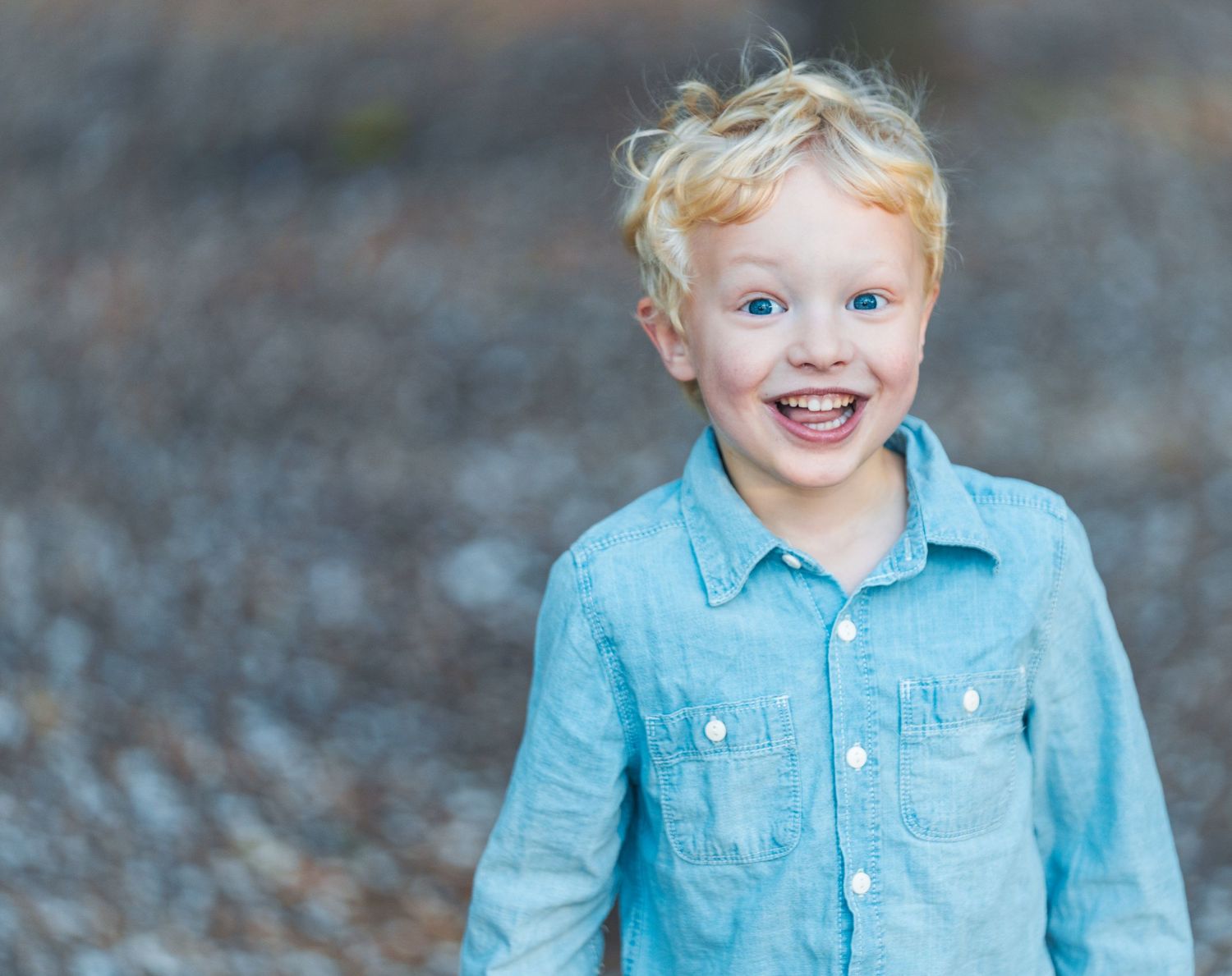 Portrait of child in blue denim shirt smiling at camera.