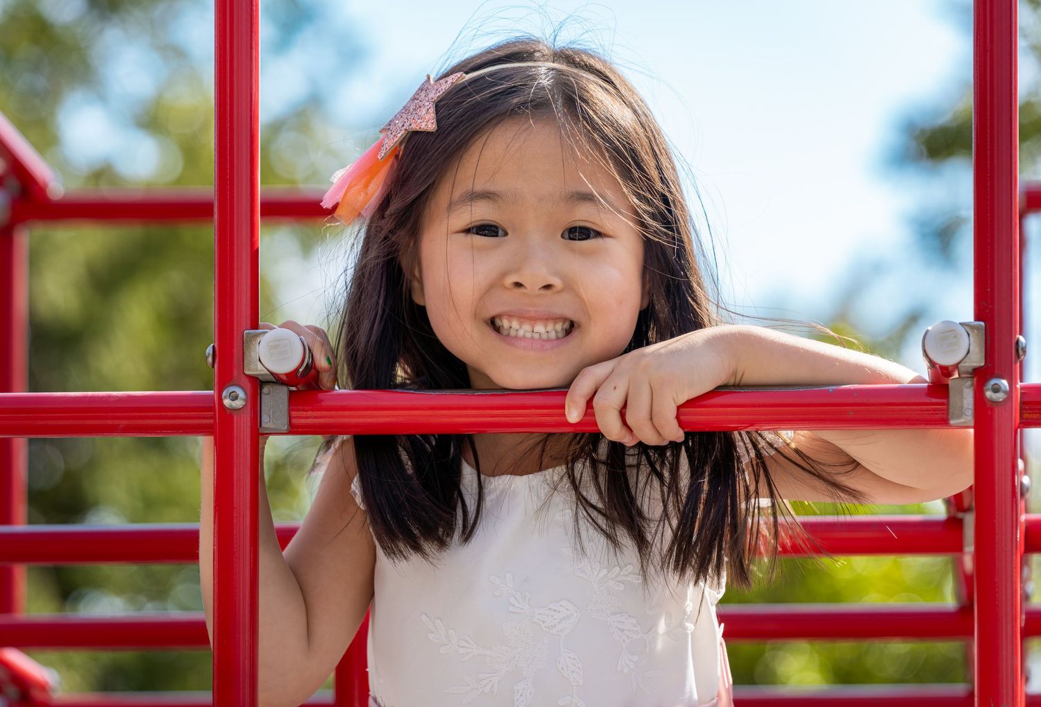Smiling young Asian girl playing on red playground equipment outdoors on a sunny day.