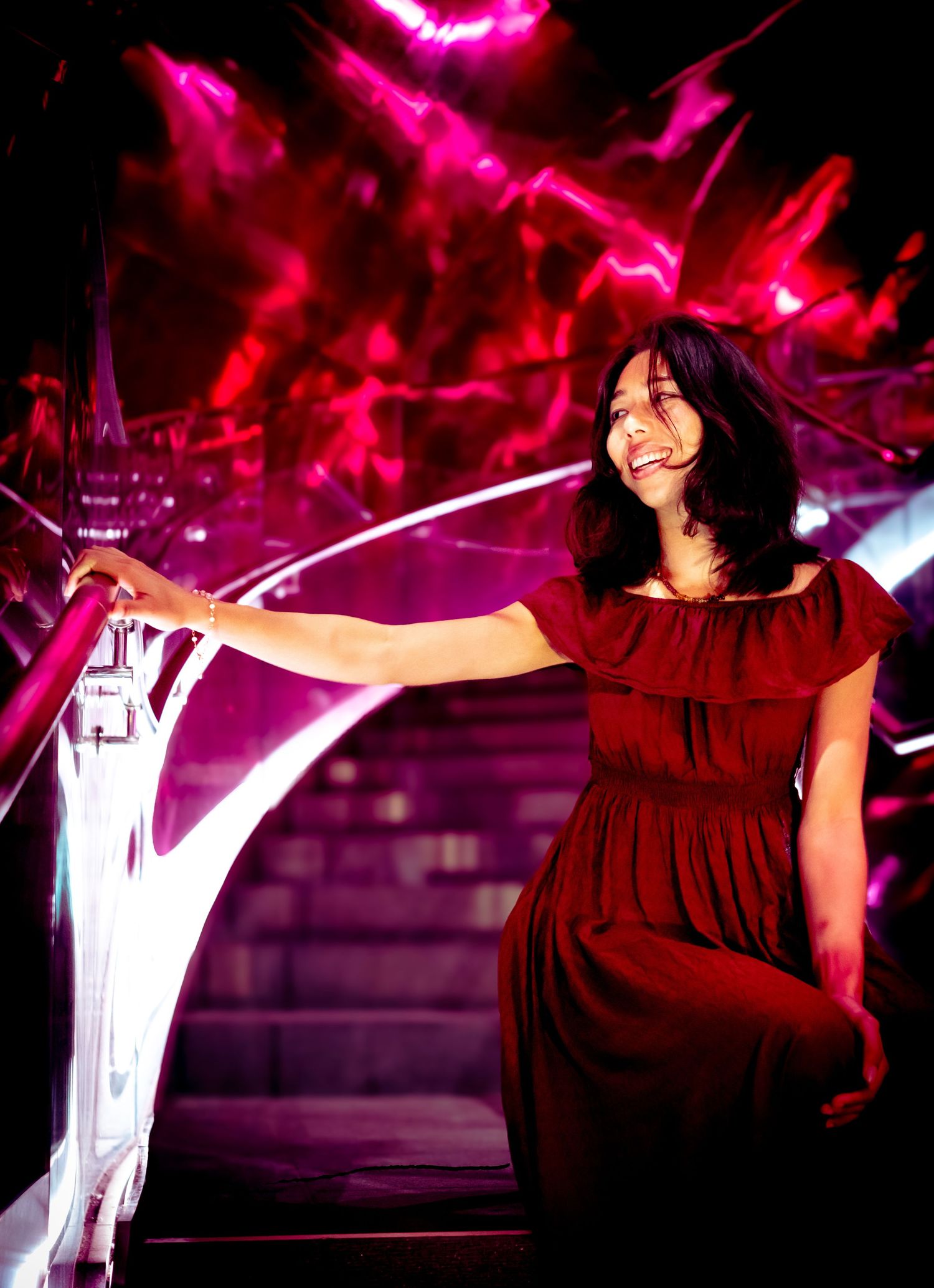 Woman in red dress posing dramatically against vibrant pink lighting and dark background.