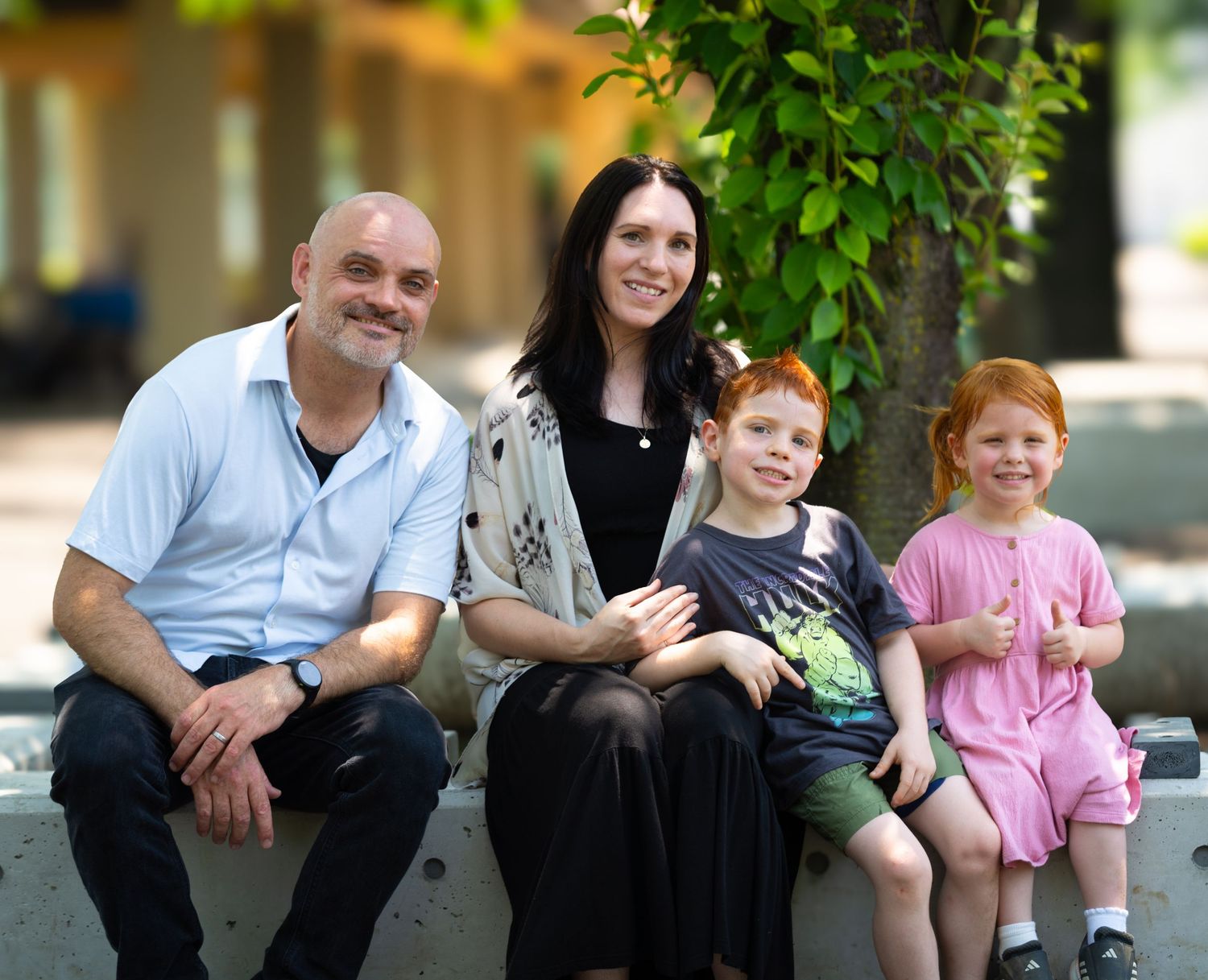 Family sitting together on outdoor stone steps surrounded by green foliage in nature setting.