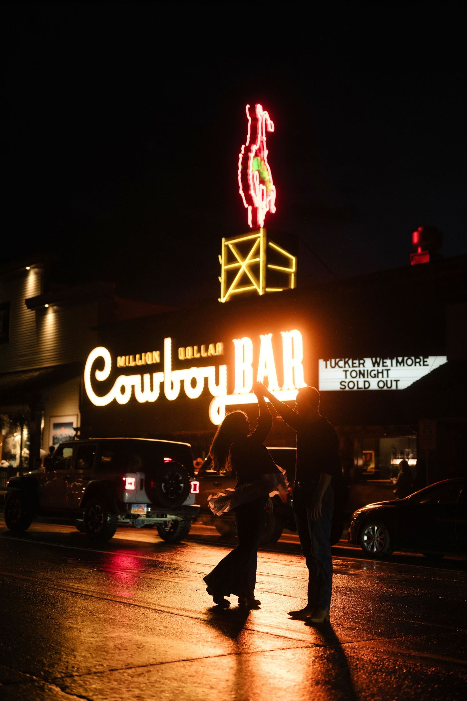 Couple dancing outside the neon-lit Million Dollar Cowboy Bar at night in Jackson Hole, Wyoming.