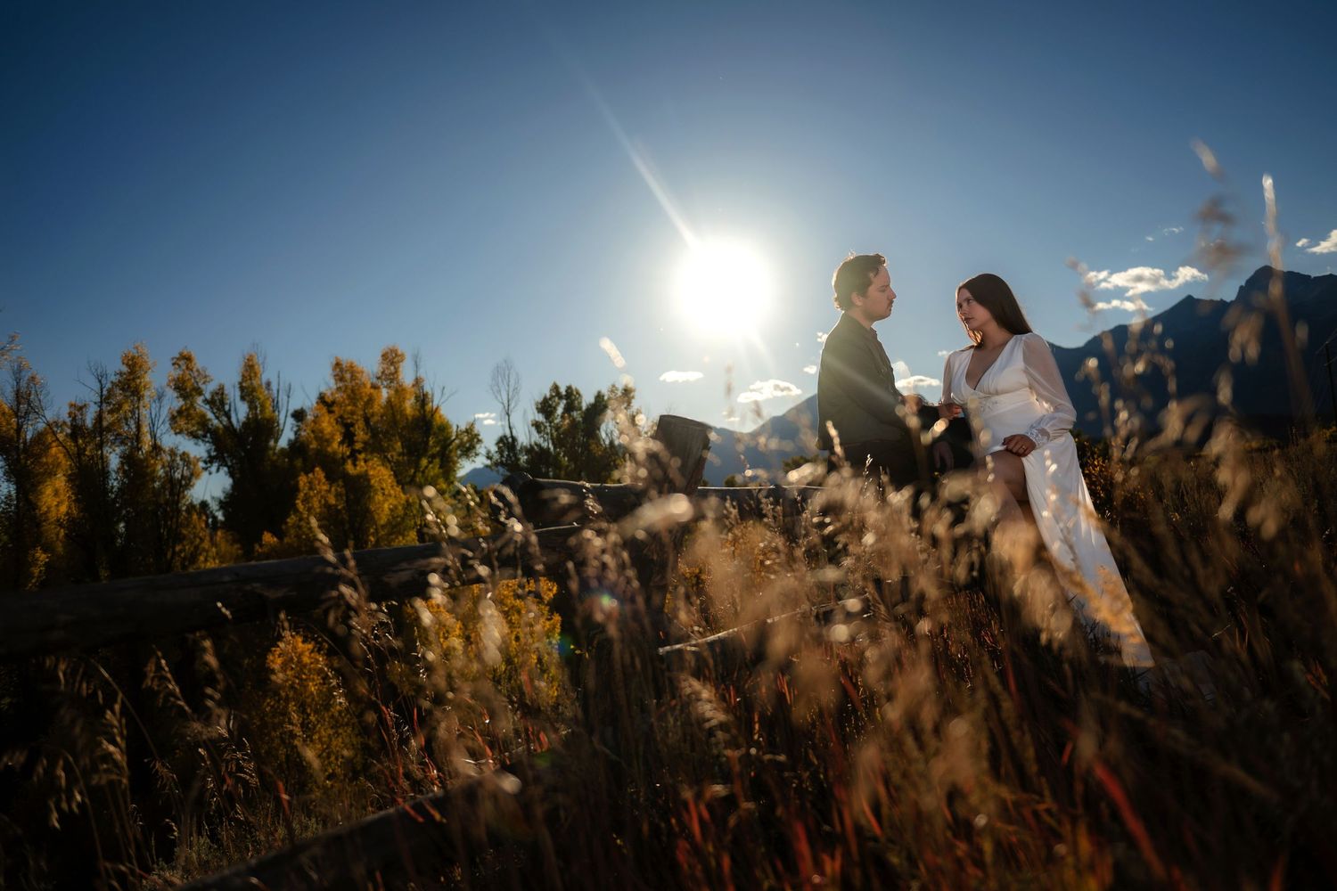 Bride and Groom standing in golden field with mountain backdrop and bright sun, surrounded by tall grass in autumn landscape in Grand Teton