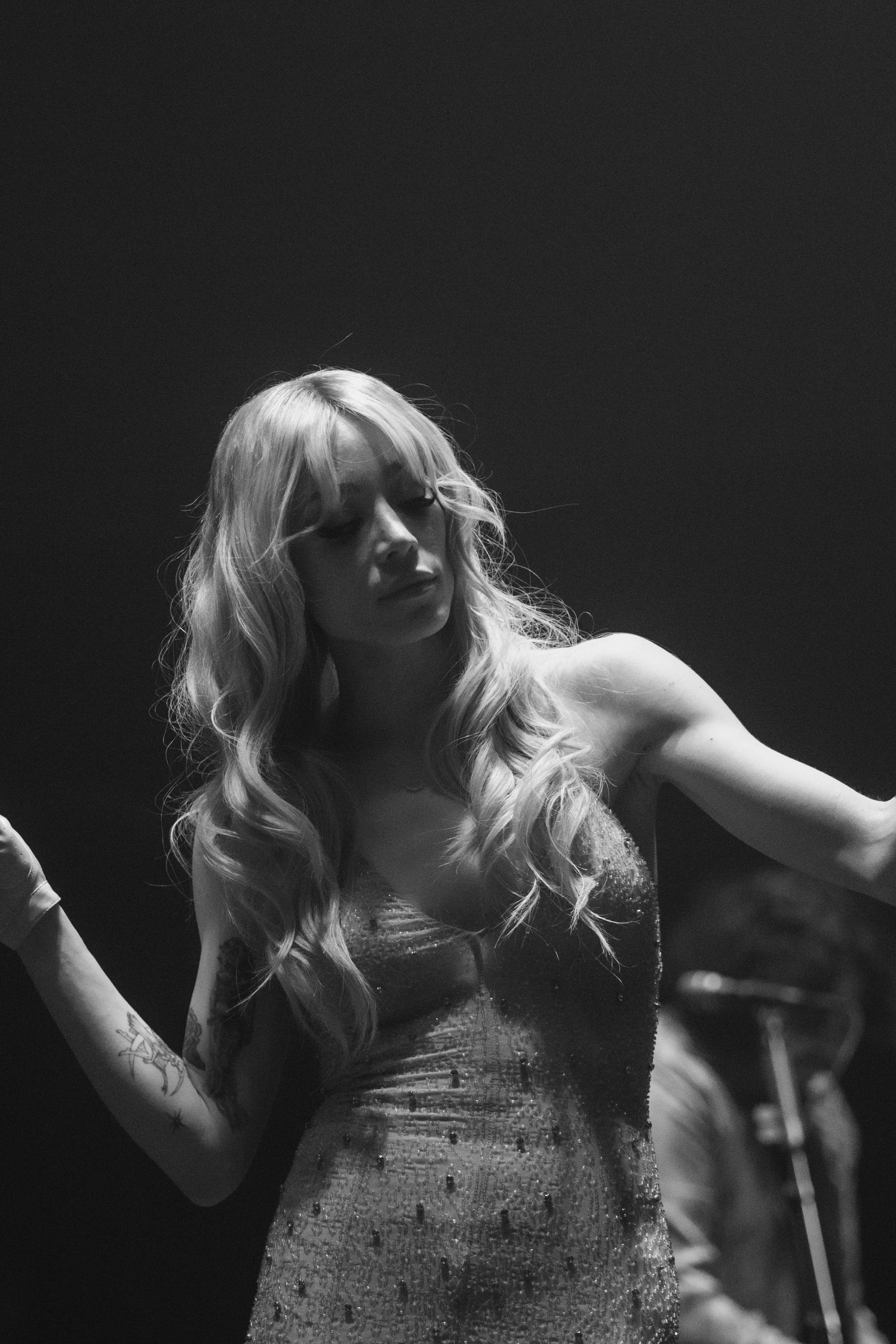Black and white photo of a blonde woman in a sequined dress performing on stage under dramatic lighting.