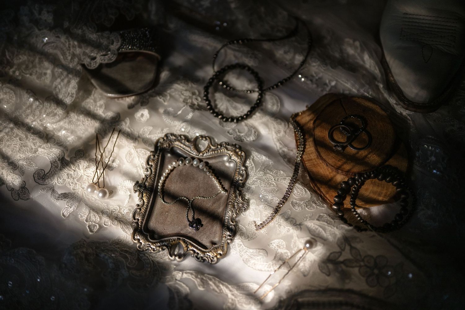 Vintage jewelry display with ornate mirror, bracelets, hair pins, and accessories arranged on white lace fabric in moody lighting.
