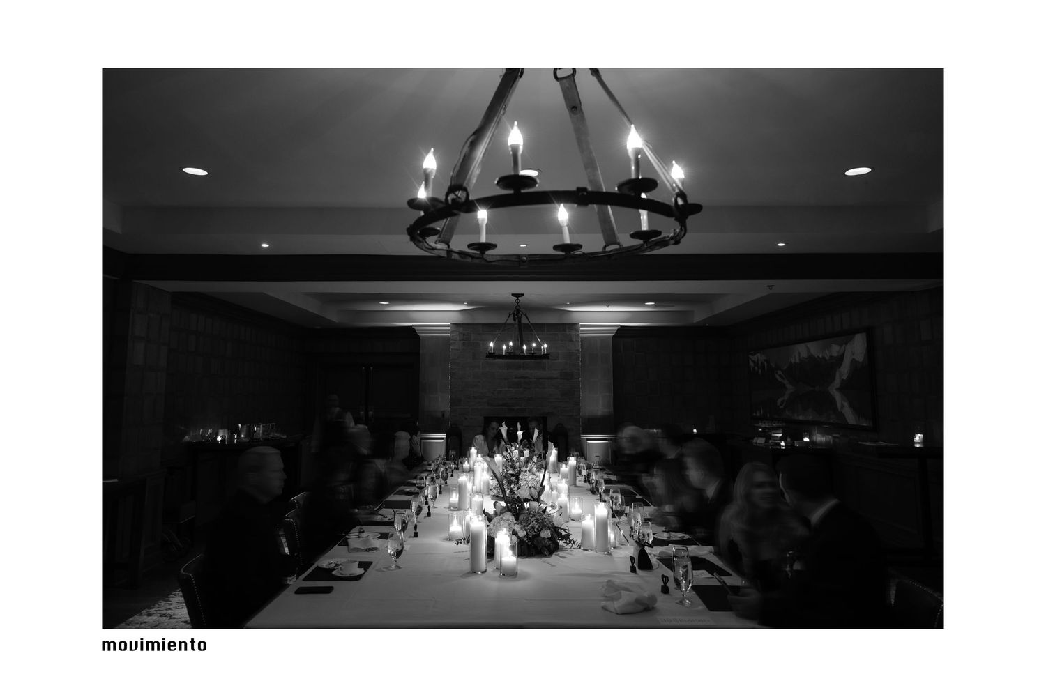 Elegant candlelit wedding reception dinner in a dark banquet hall with chandelier lighting.