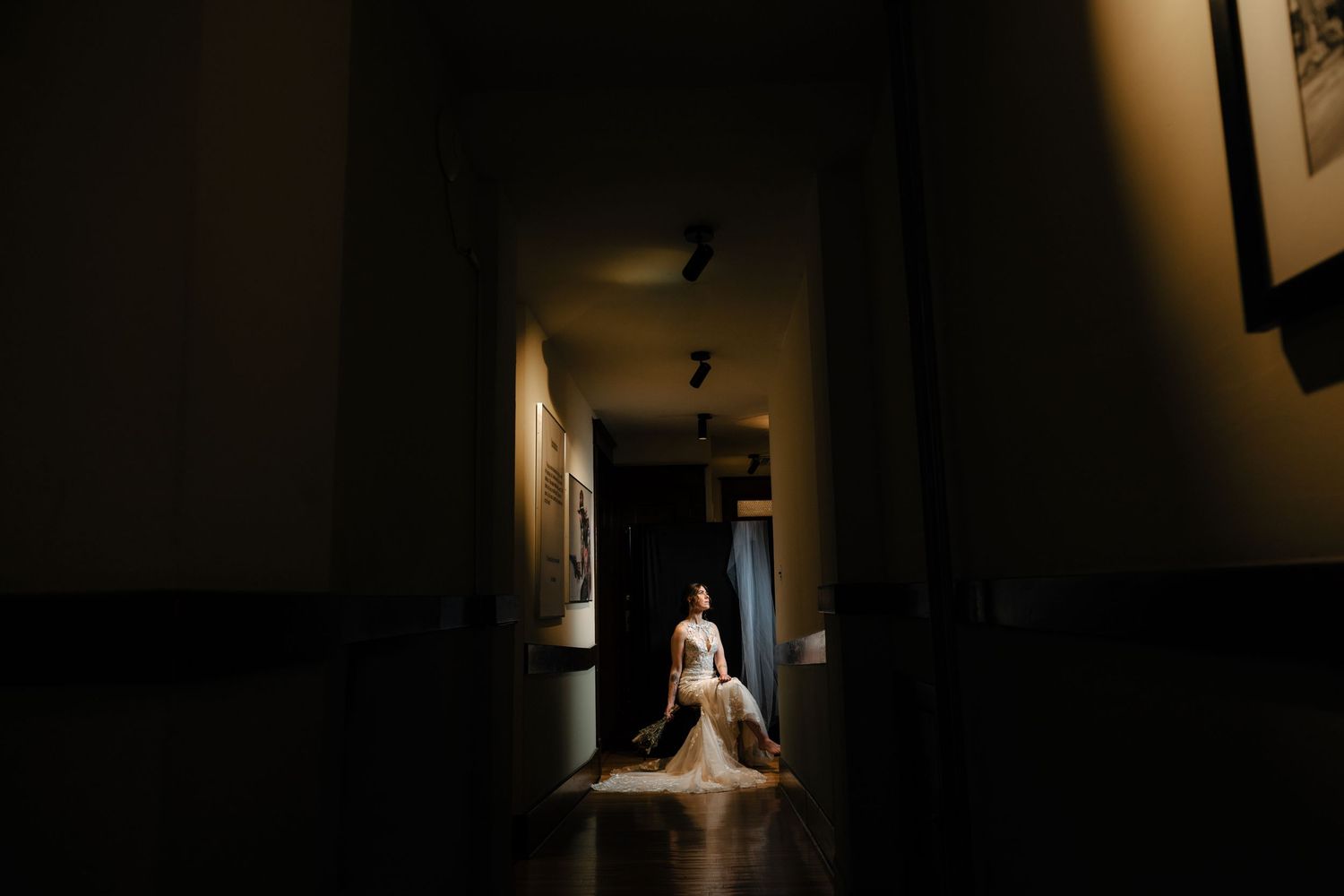 Bride in wedding gown sitting gracefully in a dramatic, dimly lit hallway with warm light highlighting her dress. Livingston Montana Wedding