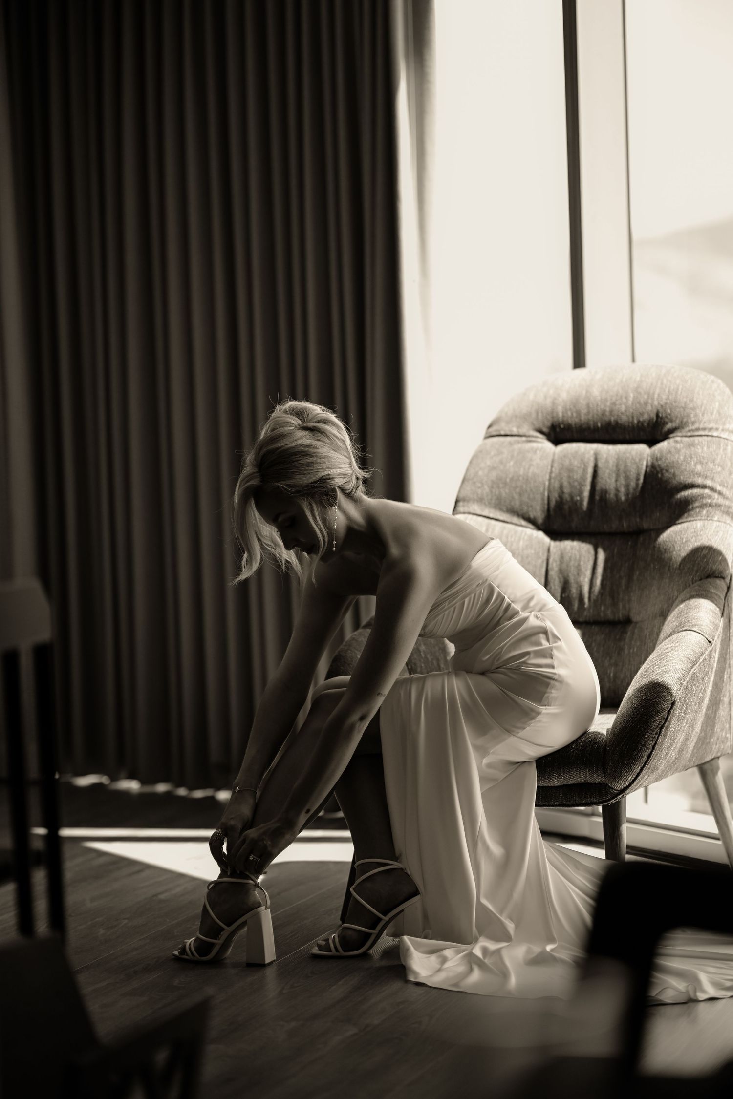 A woman in a white dress sits in a chair, her head bowed down.