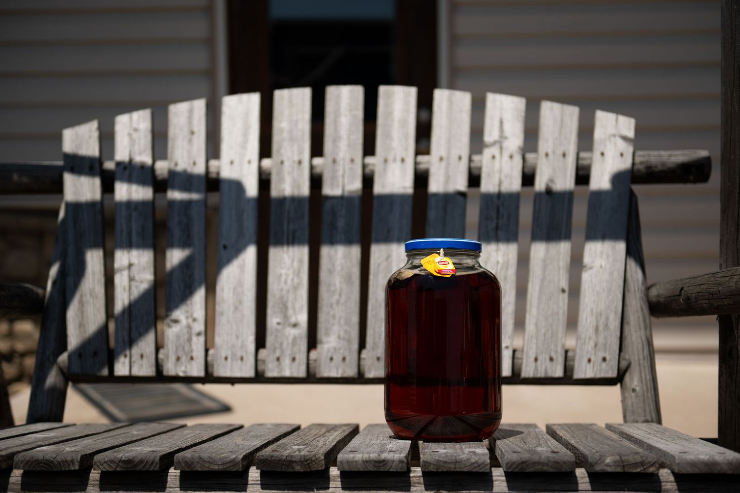 A glass of dark liquid on a weathered white wooden bench casting long shadows.