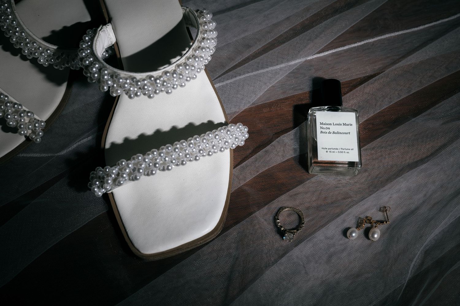A wedding dress, veil, and perfume bottle are arranged on a wooden surface.