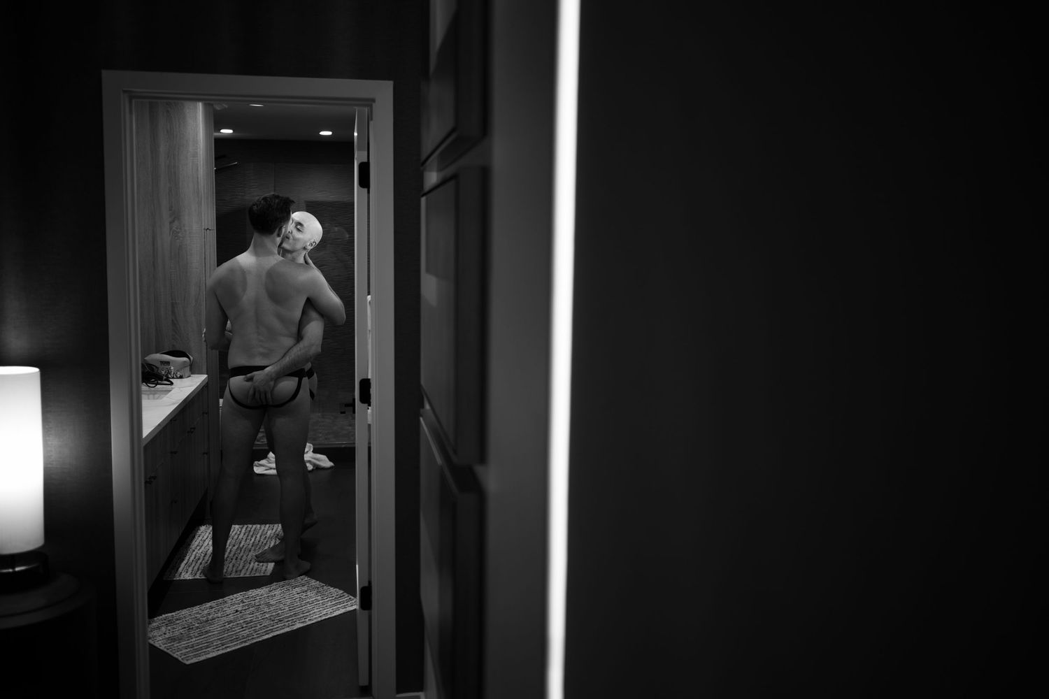 Black and white photo of a person standing in a dimly lit bathroom doorway at night.