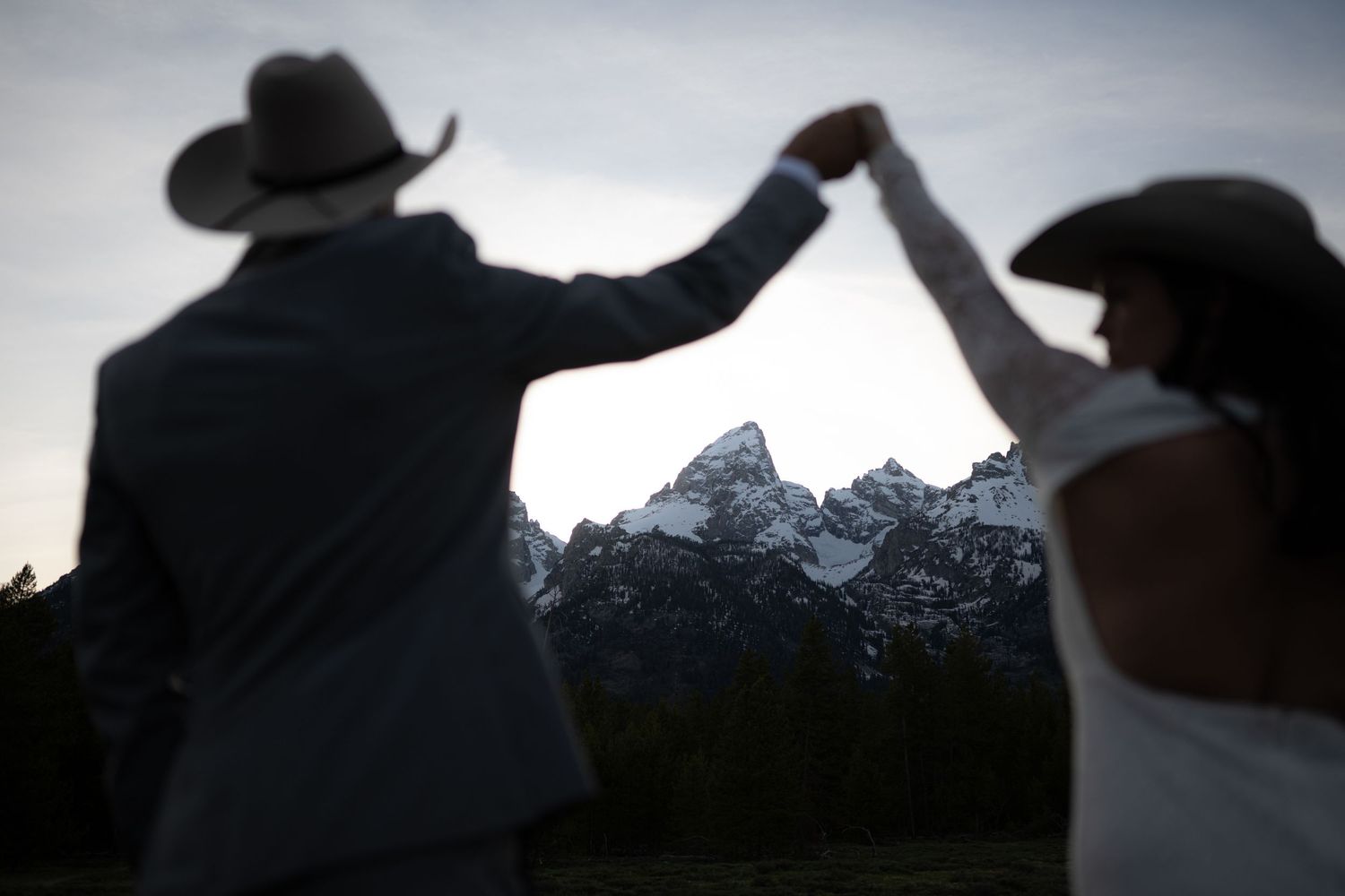 Silhouette of a couple in cowboy hats dancing before the Grand Teton mountains at dusk on their wedding day.