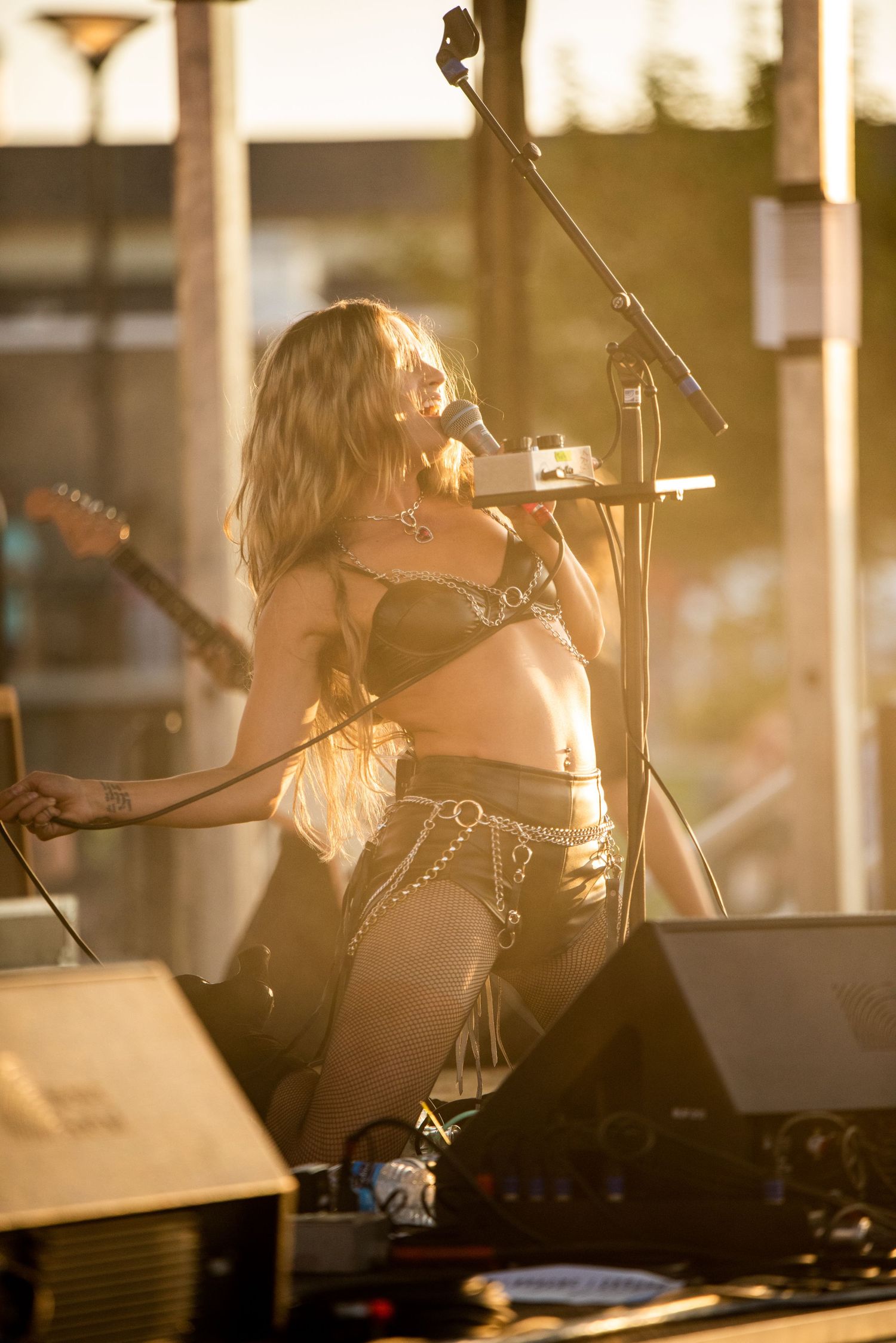A performer sings passionately on stage in a golden-lit concert setting with musical equipment visible around them.