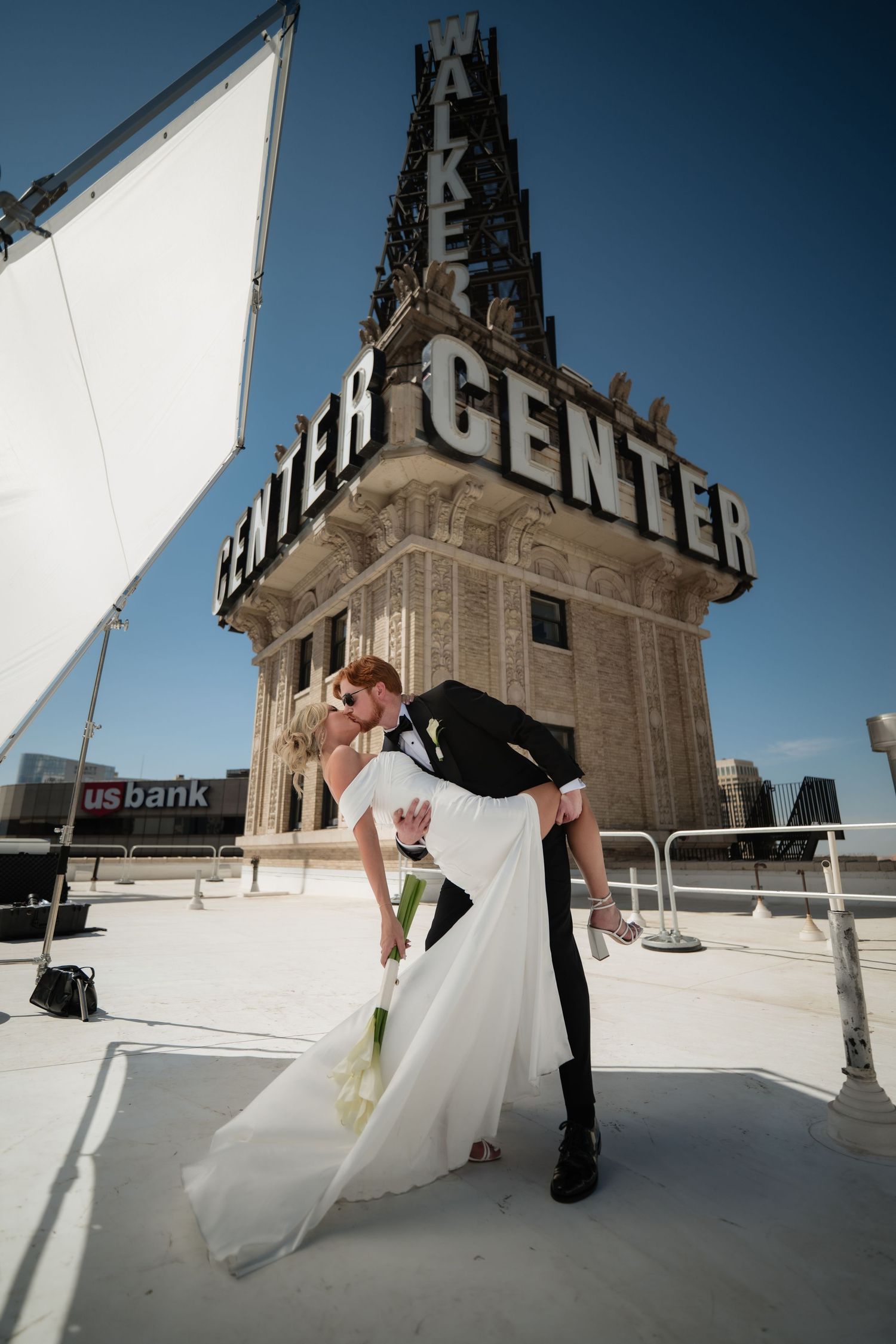 A bride and groom posing in front of a large sign for a venue.