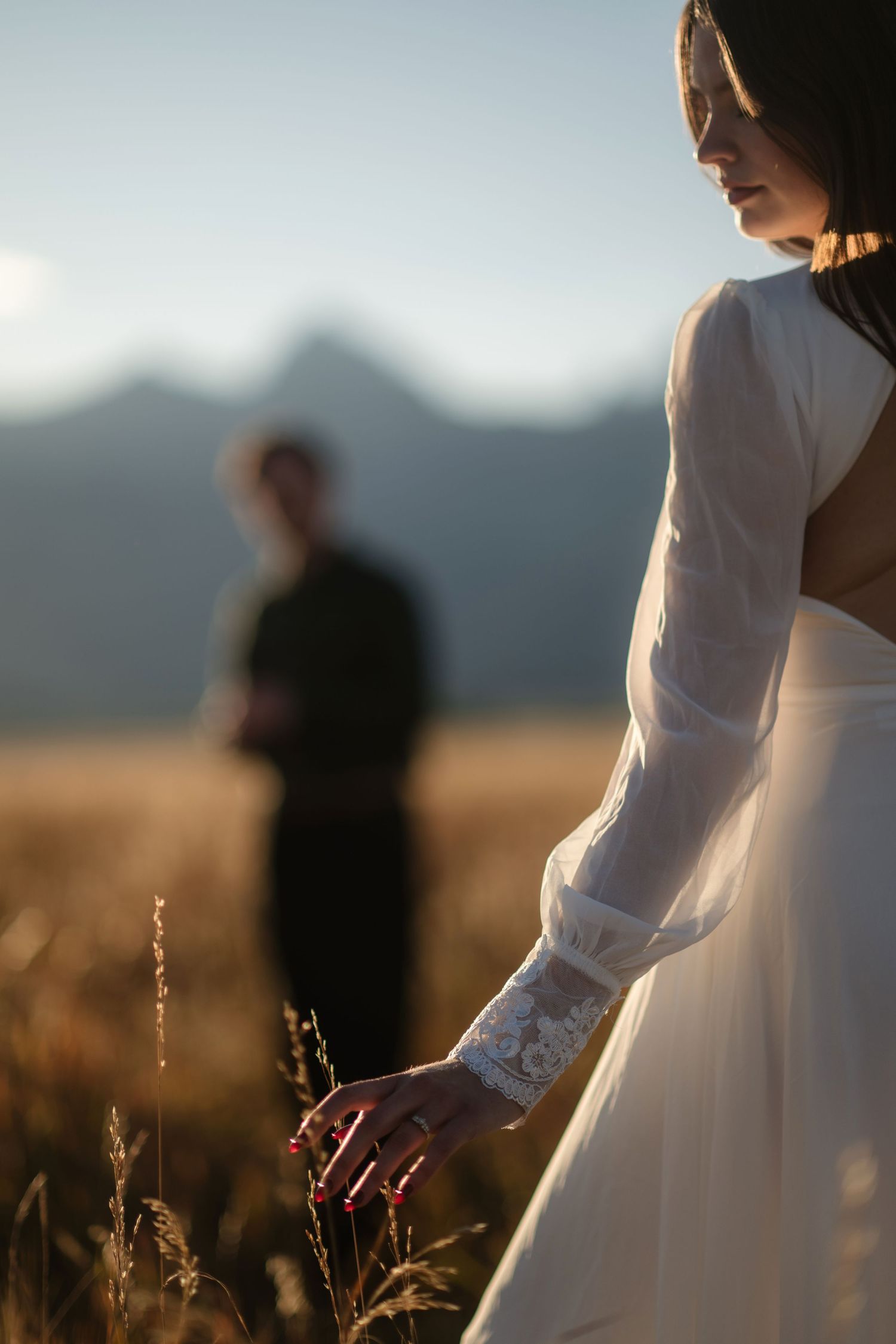 A silhouette of a bride standing in a field with mountains in the background.