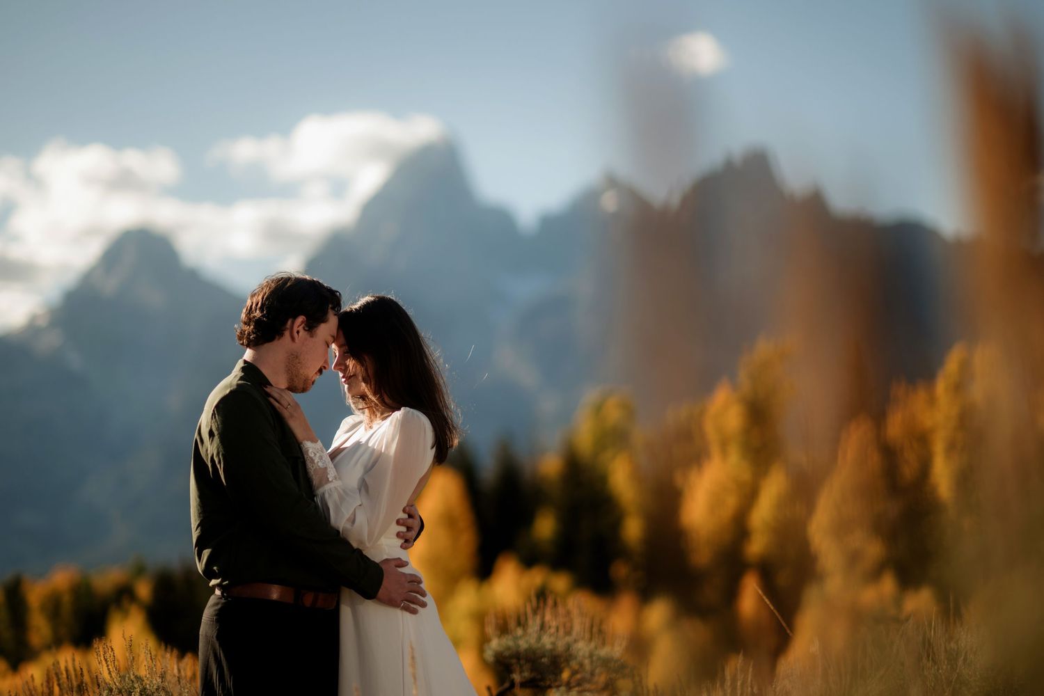 A couple embracing in a field with mountains in the background.