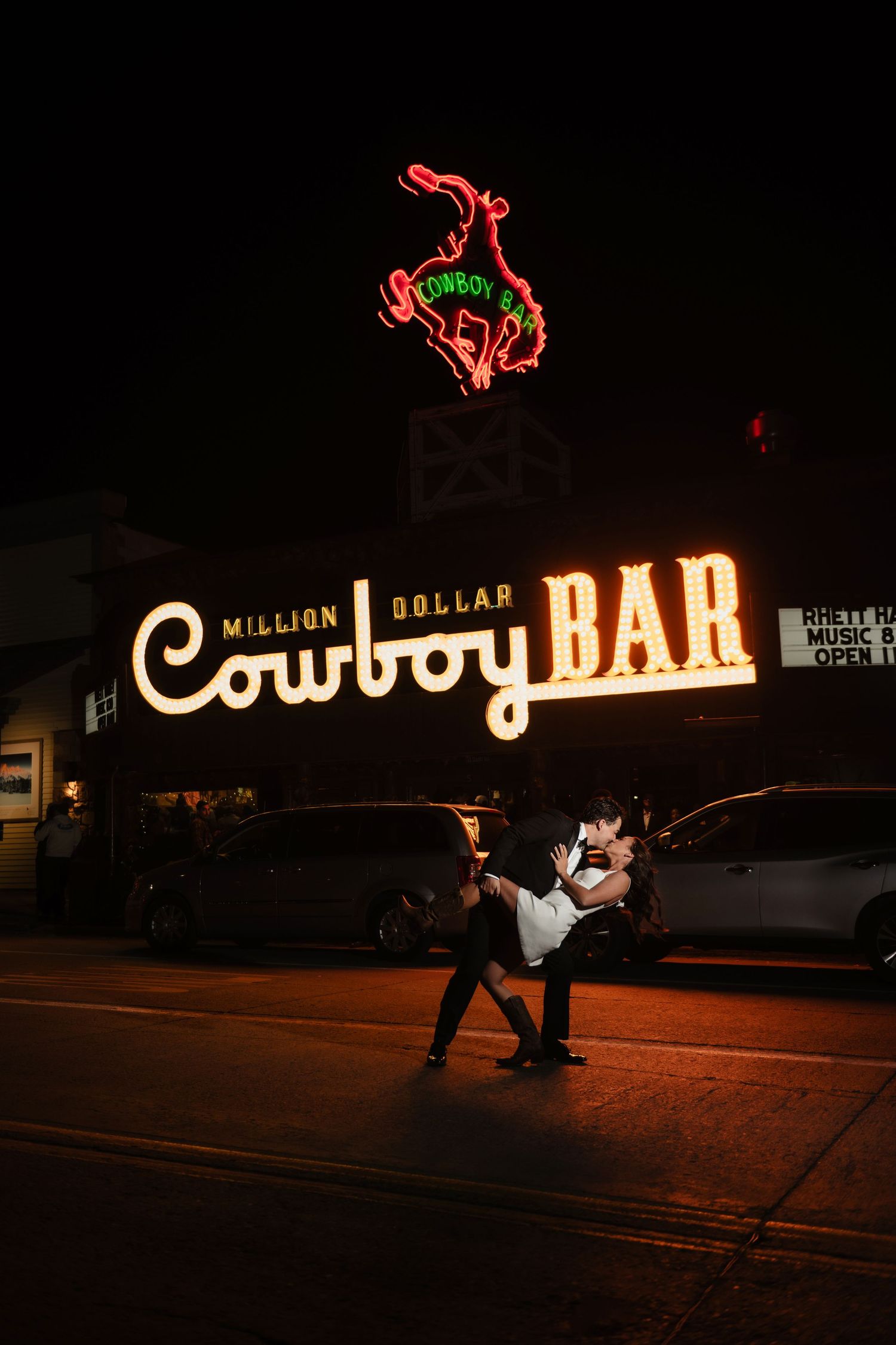 Couple dancing in front of the iconic Million Dollar Cowboy Bar neon sign at night in Jackson.