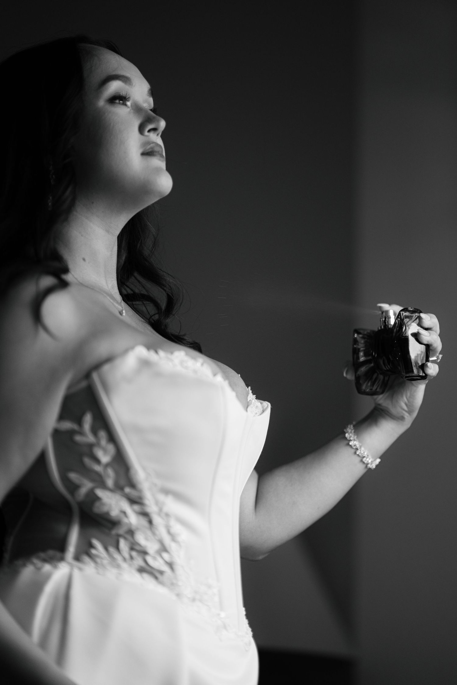 A woman in a white dress holds a camera, looking pensive in a dramatic black and white portrait.