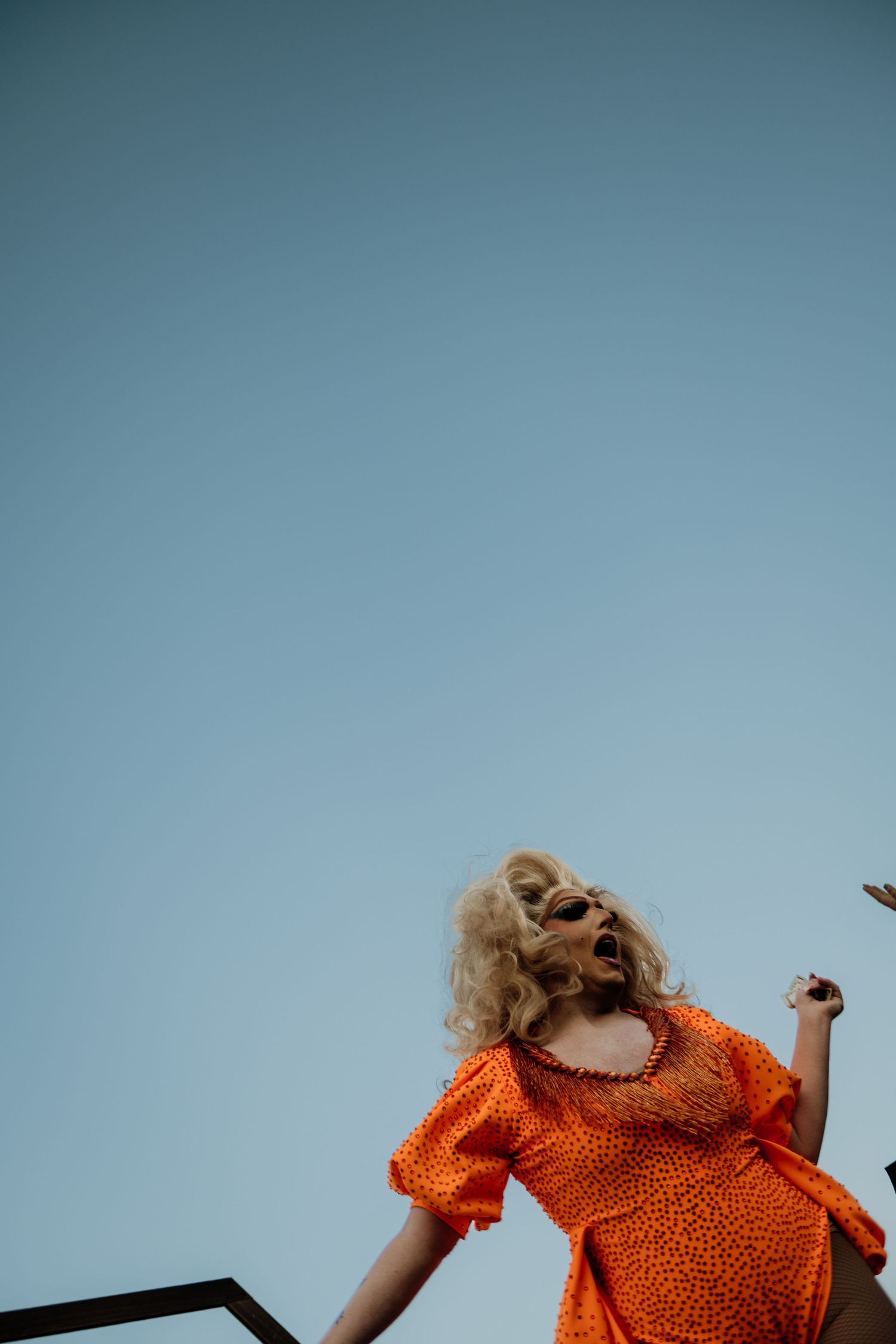 Person in orange polka dot dress with blonde hair dancing energetically against a clear blue sky.