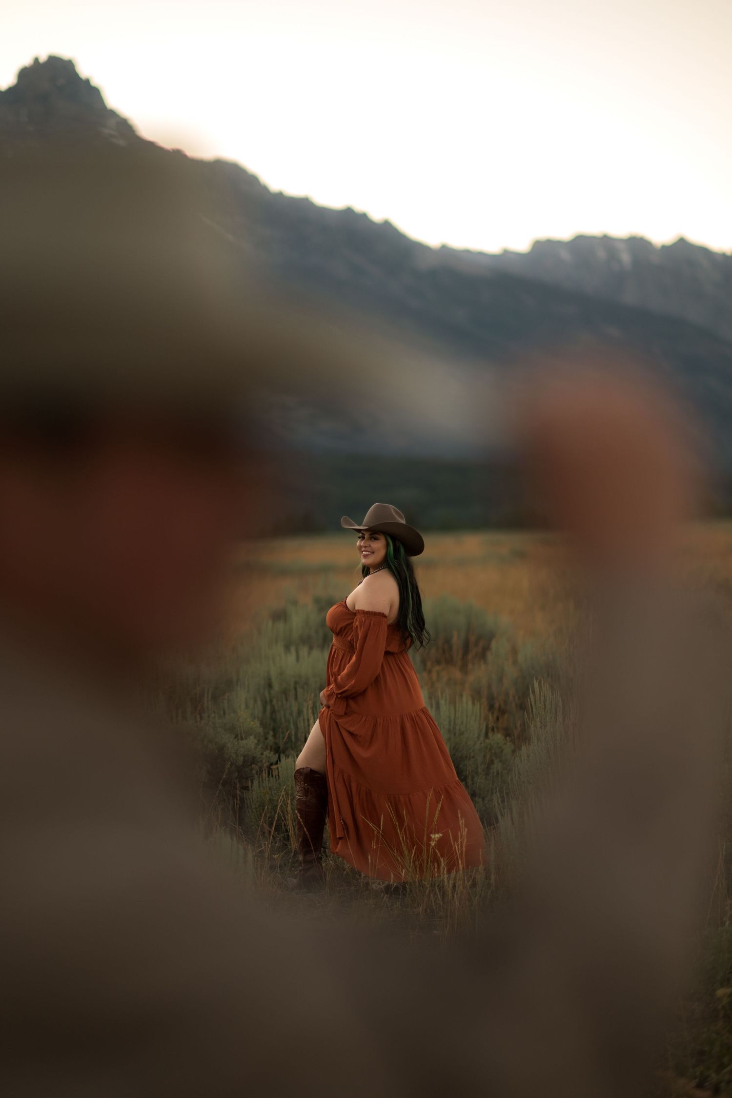 A woman in a flowing, red dress stands in a vast, mountainous field.