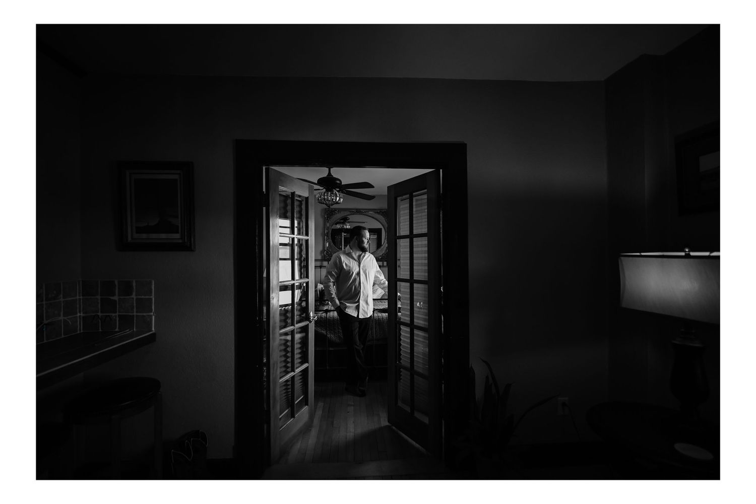 Black and white photo of a couple embracing in a doorway, framed by French doors in a dimly lit room.