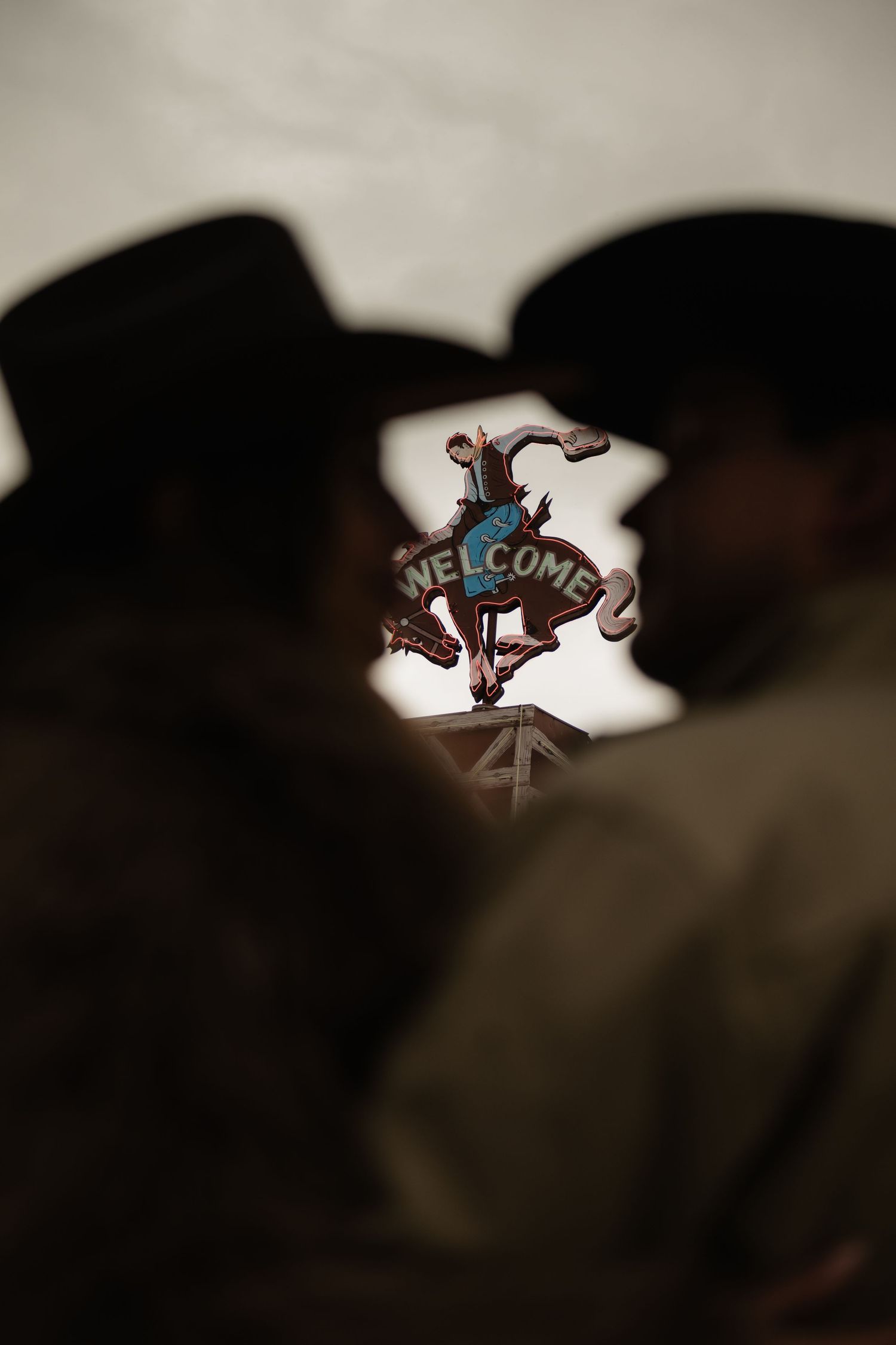 Two silhouetted cowboys kissing beneath a colorful Welcome sign with a bucking bronco at a western venue.