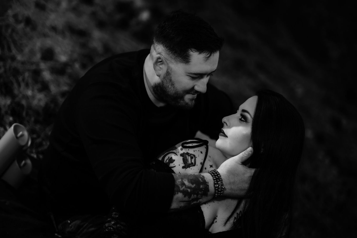 A couple embrace and look affectionately at each other in a natural, outdoor setting.