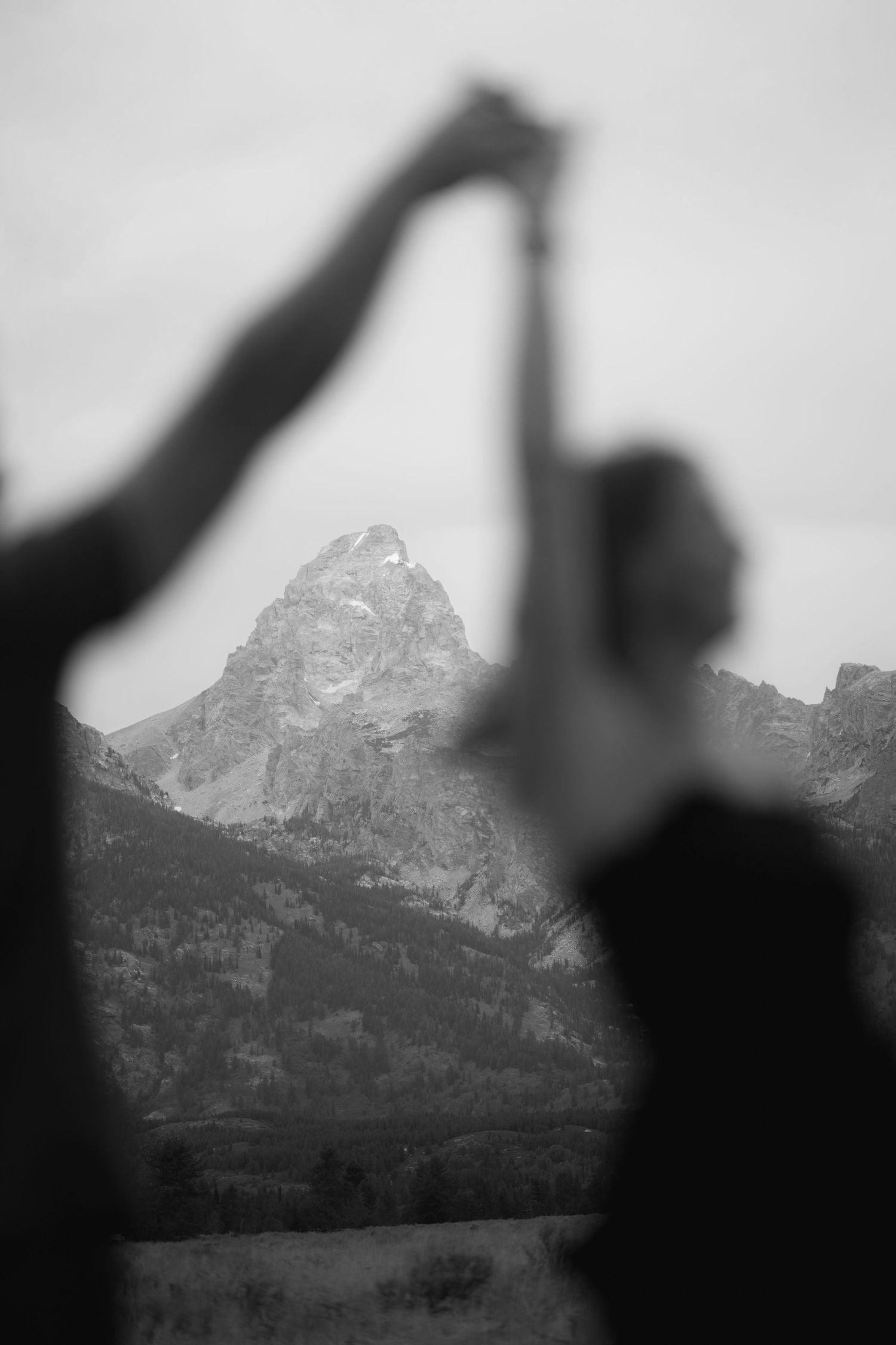 Black and white photo of couple holding hands with Grand Teton mountain peak in background.