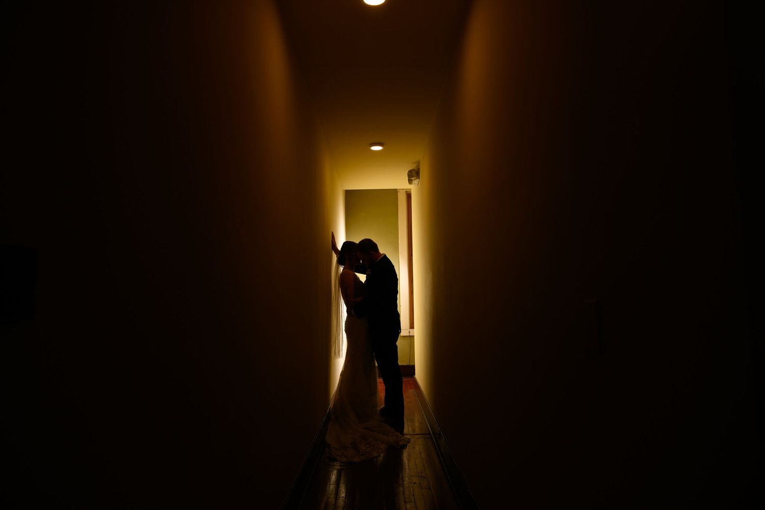 Silhouette of a couple sharing a romantic kiss in a dimly lit hallway with warm golden light.