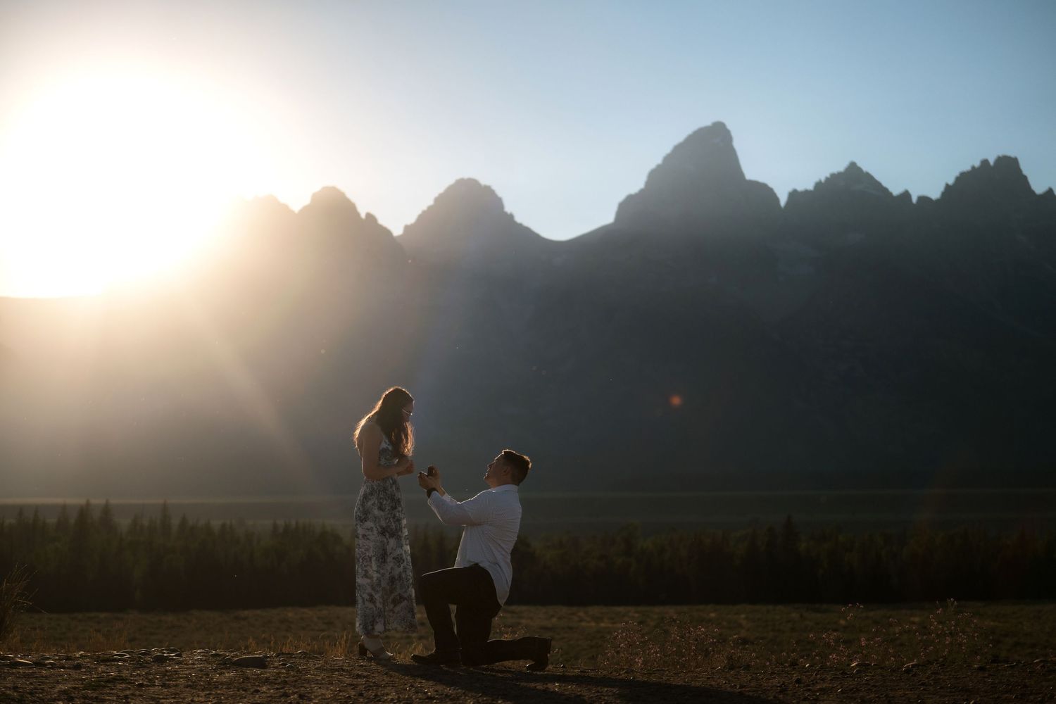 A couple stands together in a scenic mountain landscape at sunset.