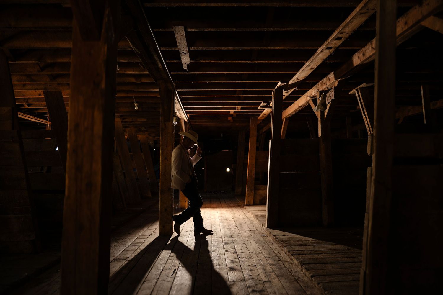 Person exploring a dark rustic wooden barn interior with dramatic lighting and aged timber beams.