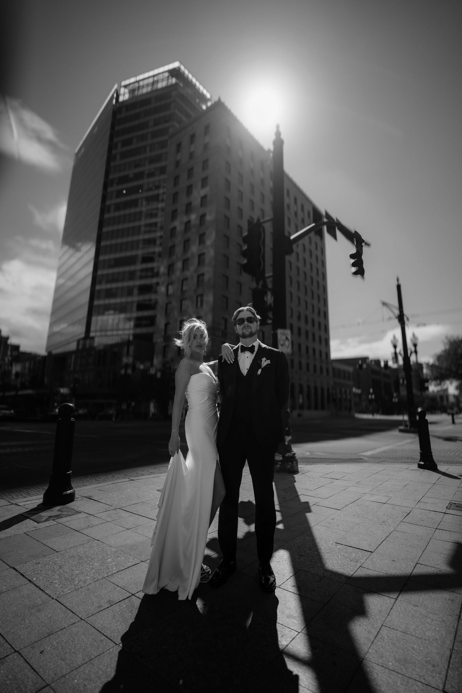 Black and white photo of a bride and groom standing on a city street corner with a tall glass building backdrop.
