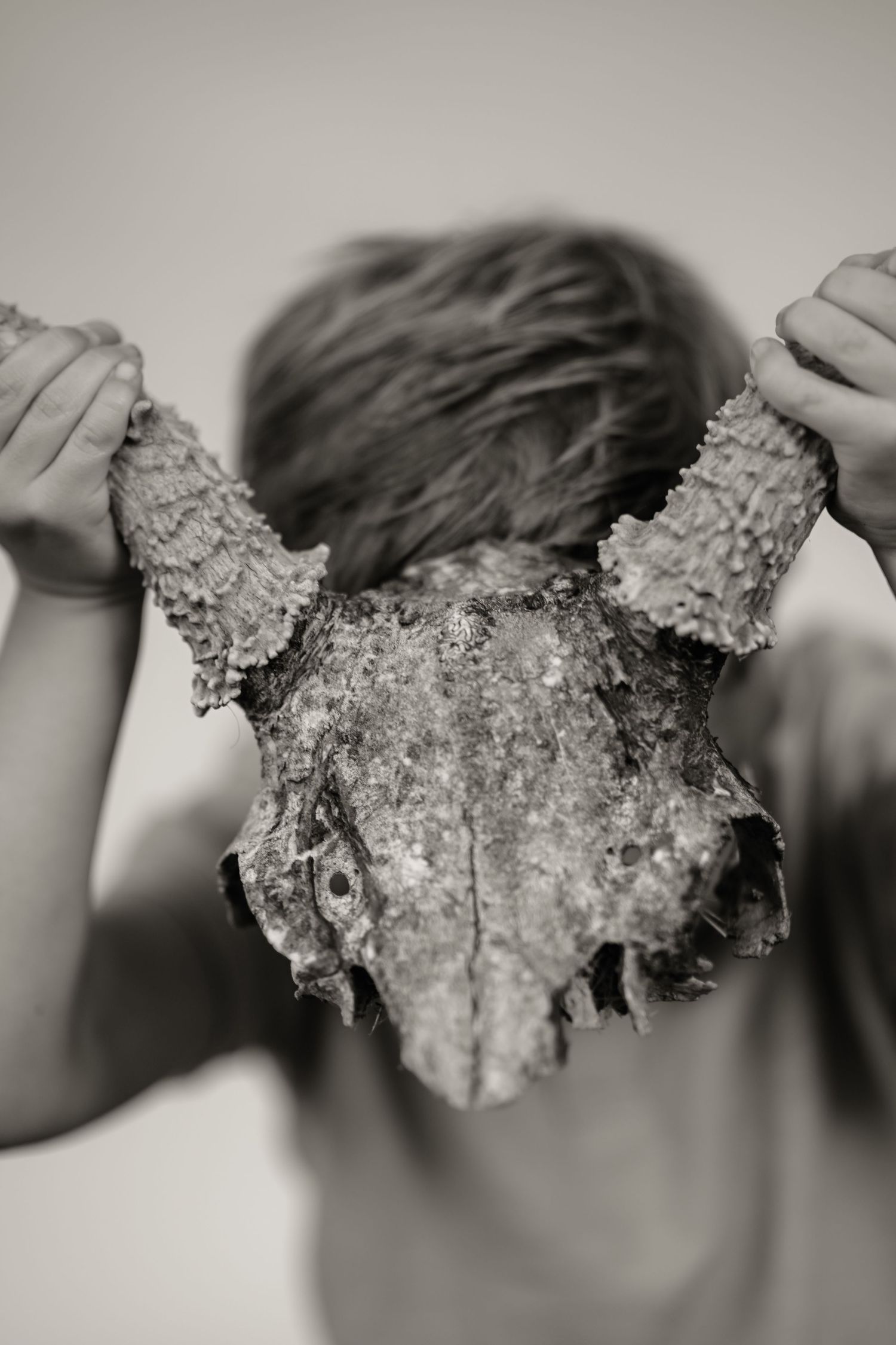 Black and white photo of child holding weathered animal skull over their face outdoors.