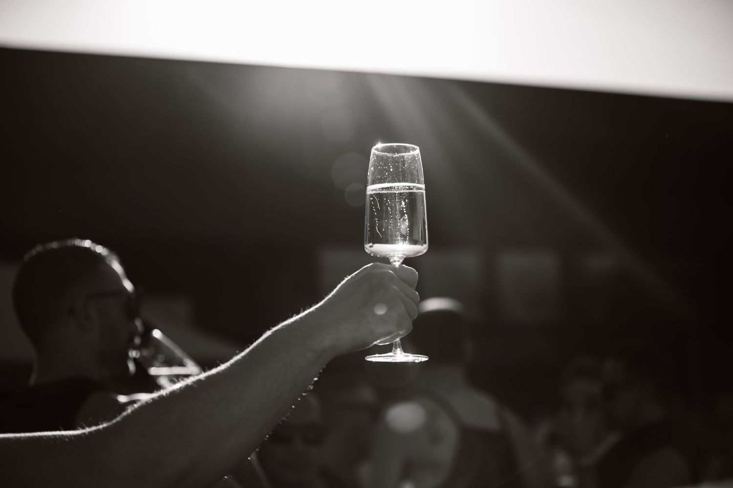 A black and white image showing a person's hand holding a glass of clear liquid, possibly water or wine.