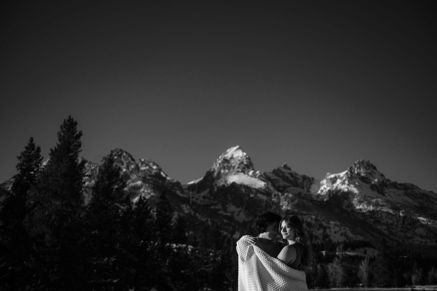 Black and white couple embracing with mountain peaks in background.