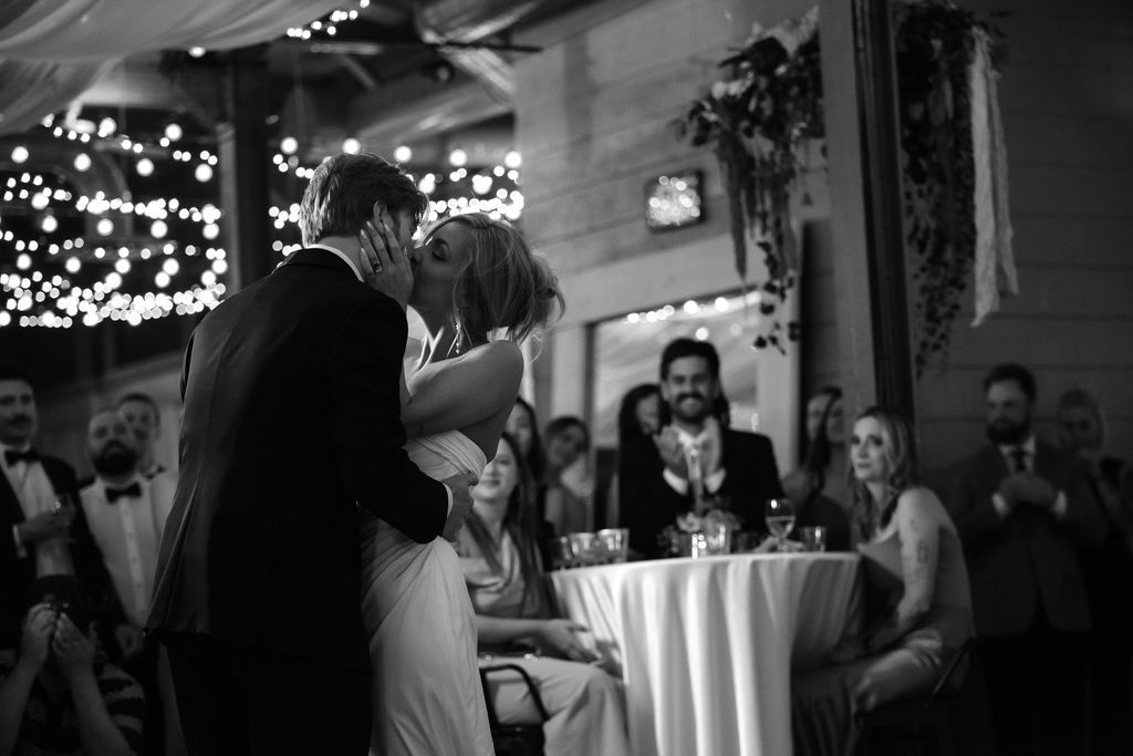 Black and white photo of a bride and groom sharing a first dance kiss at their wedding reception.