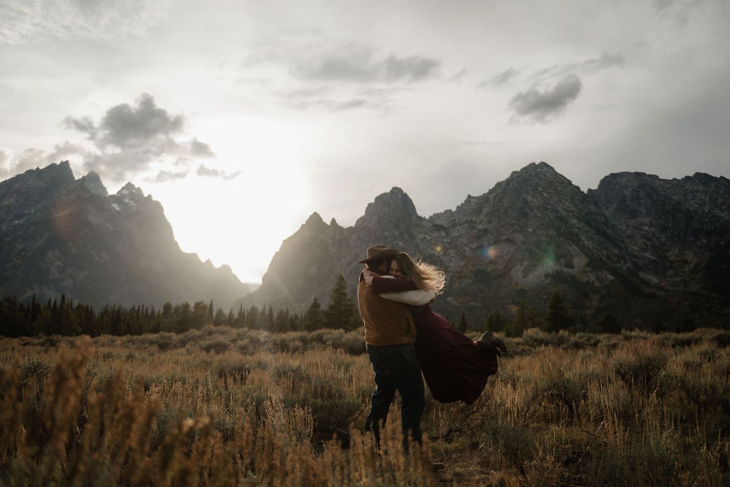 A person stands alone in a field, with snow-capped mountains in the background.