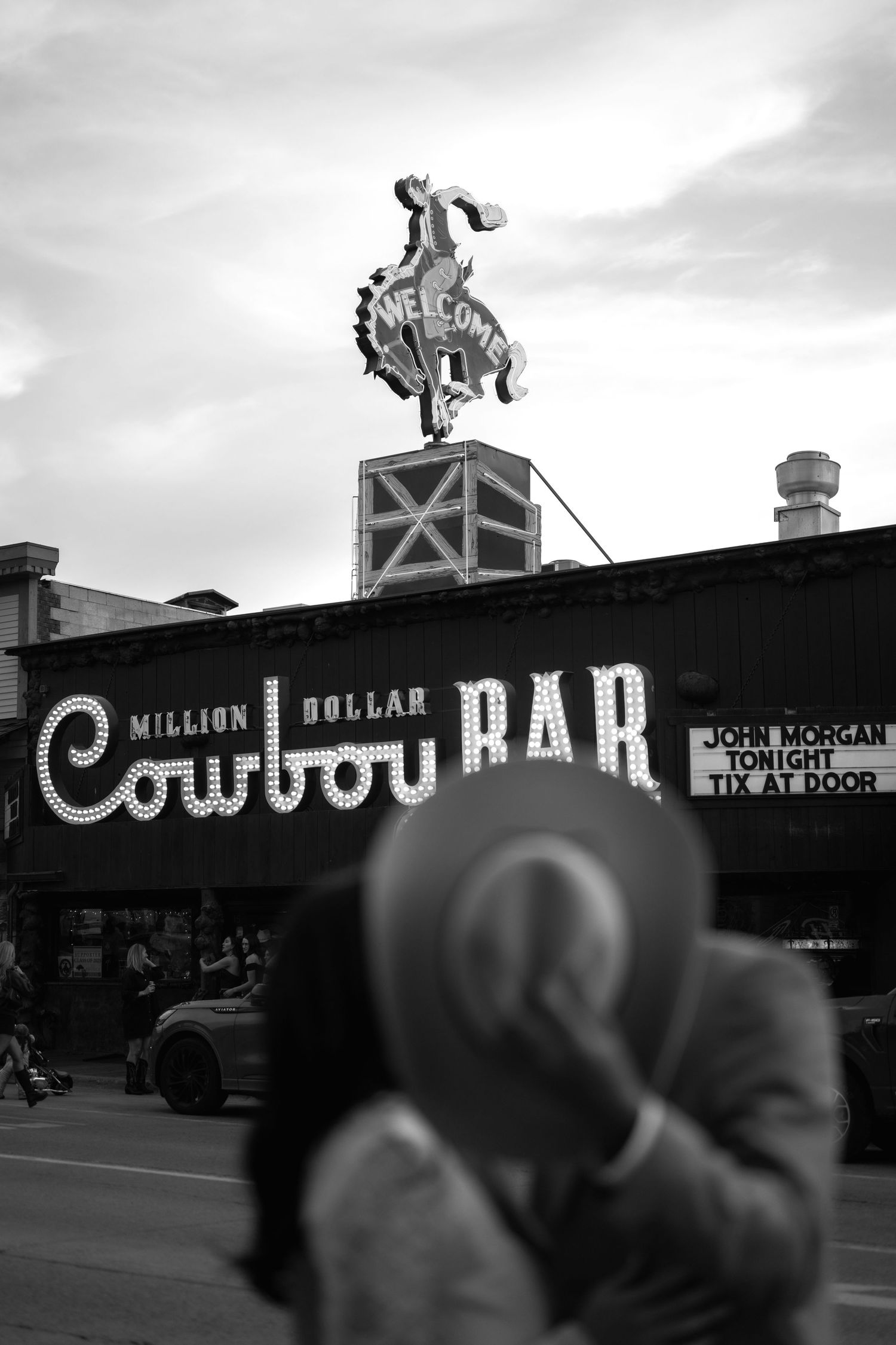 Black and white photo of the Million Dollar Cowboy Bar sign in Jackson Hole, Wyoming, with a person in a cowboy hat in foreground.