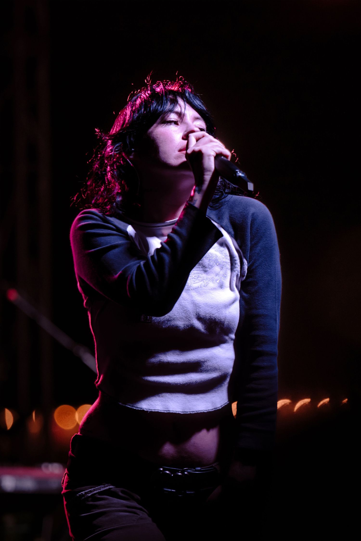 A female singer performs on stage, holding a microphone under dramatic red and purple stage lighting.