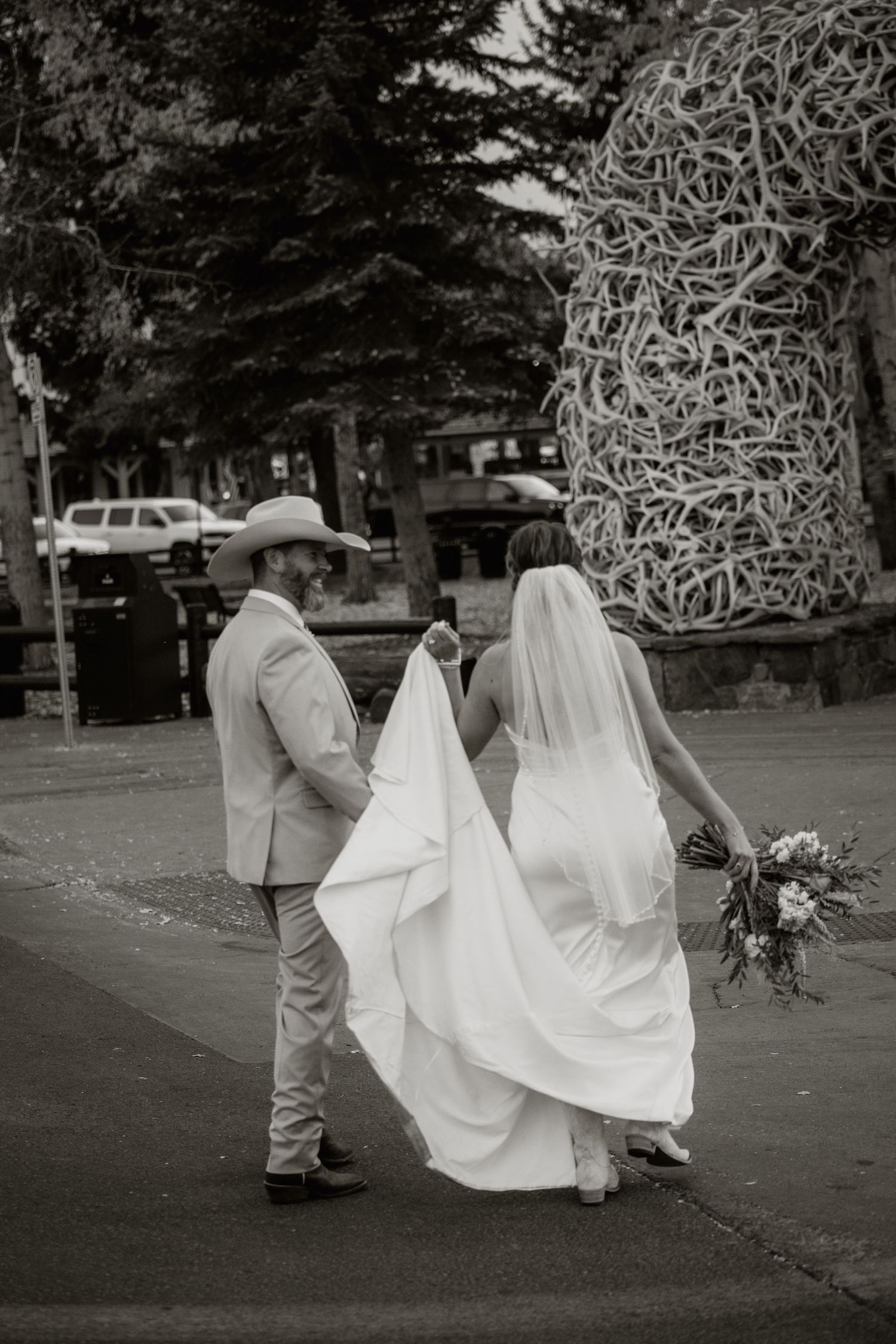 A bride and groom walk together down a city street, with a neon sign in the background.