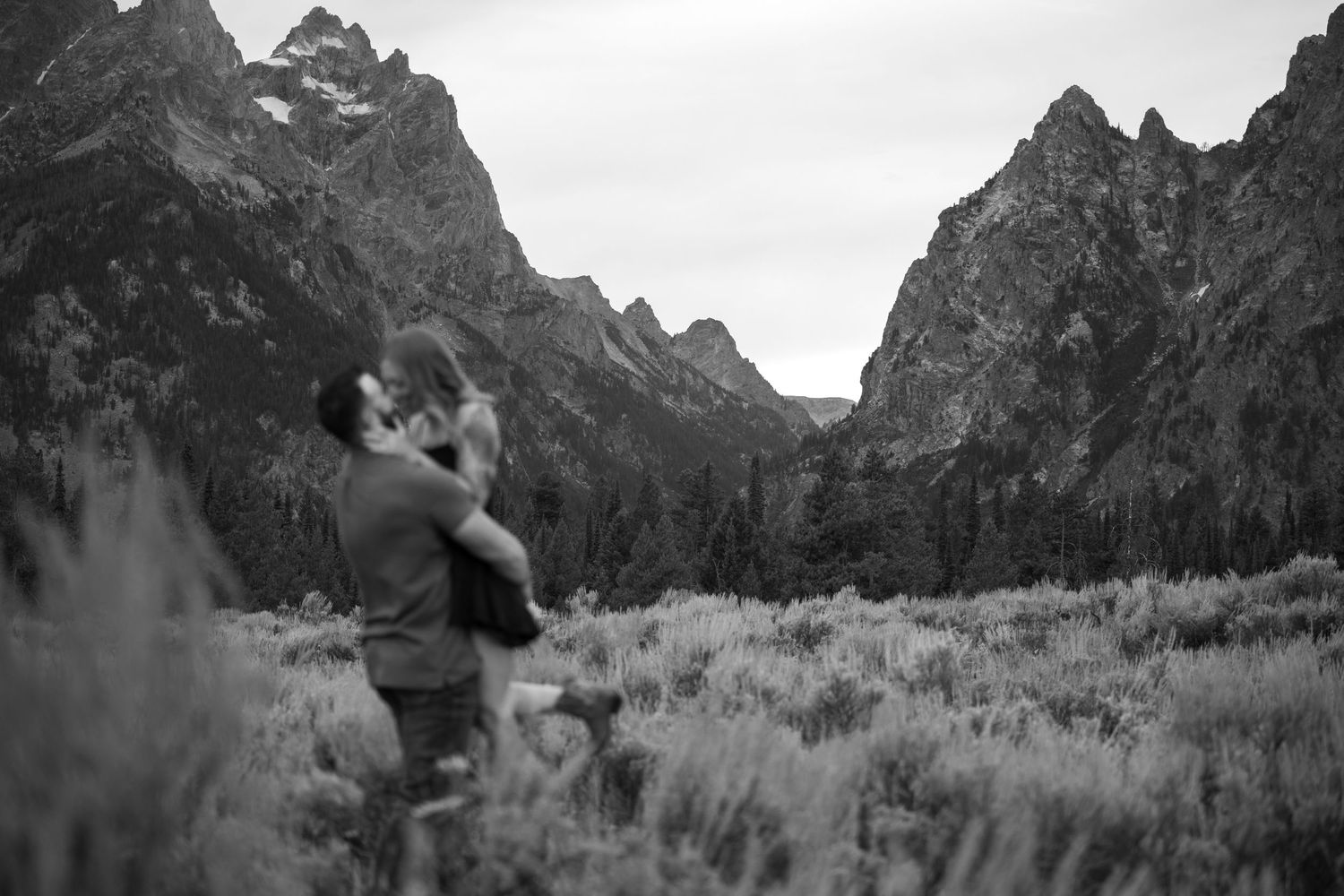 Couple embracing in a black and white photo with dramatic Grand Teton mountain peaks in the background.