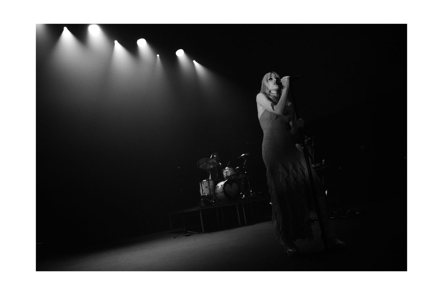 Black and white photo of a lone performer on stage under dramatic spotlights during a live concert.