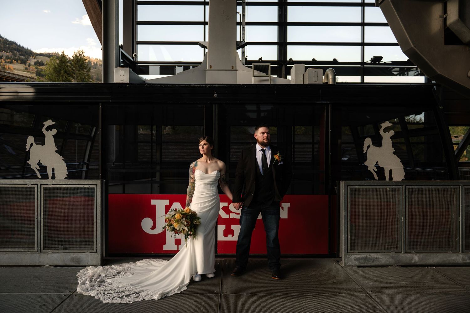 A bride and groom stand together in front of a large industrial building.