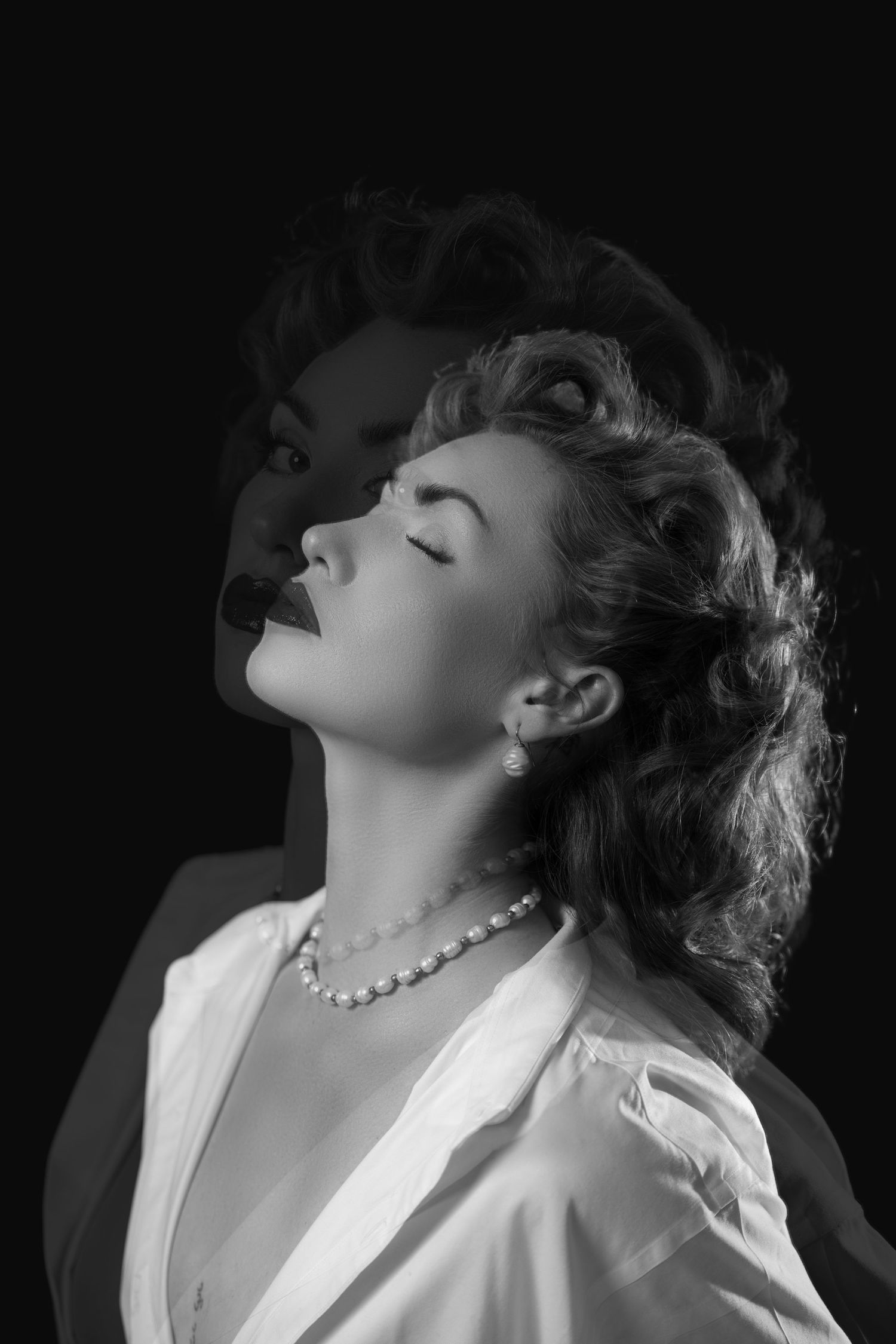 Black and white vintage portrait of a woman in pearl necklace with dramatic film noir lighting.