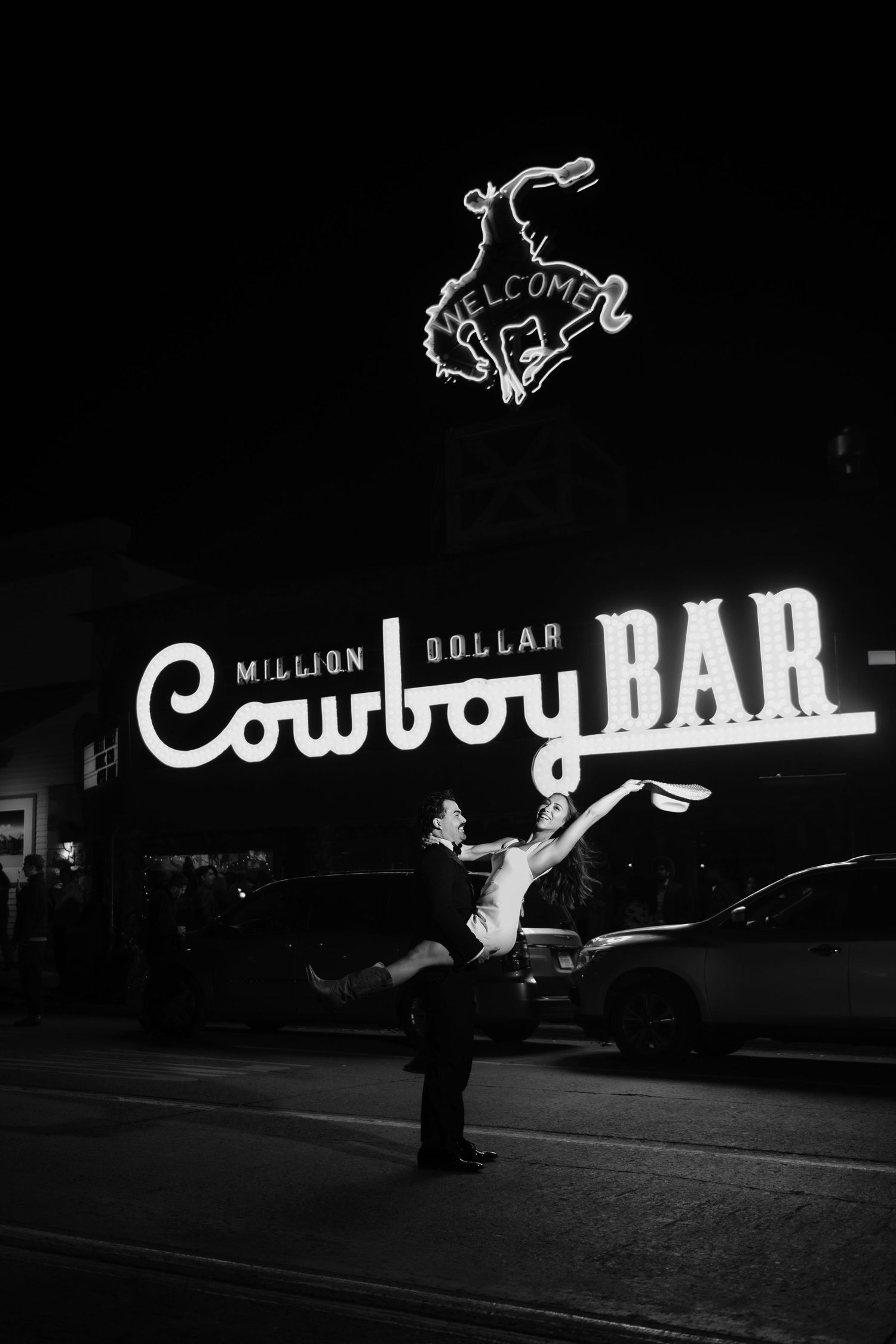 Couple dancing outside the Million Dollar Cowboy Bar neon sign at night in black and white.