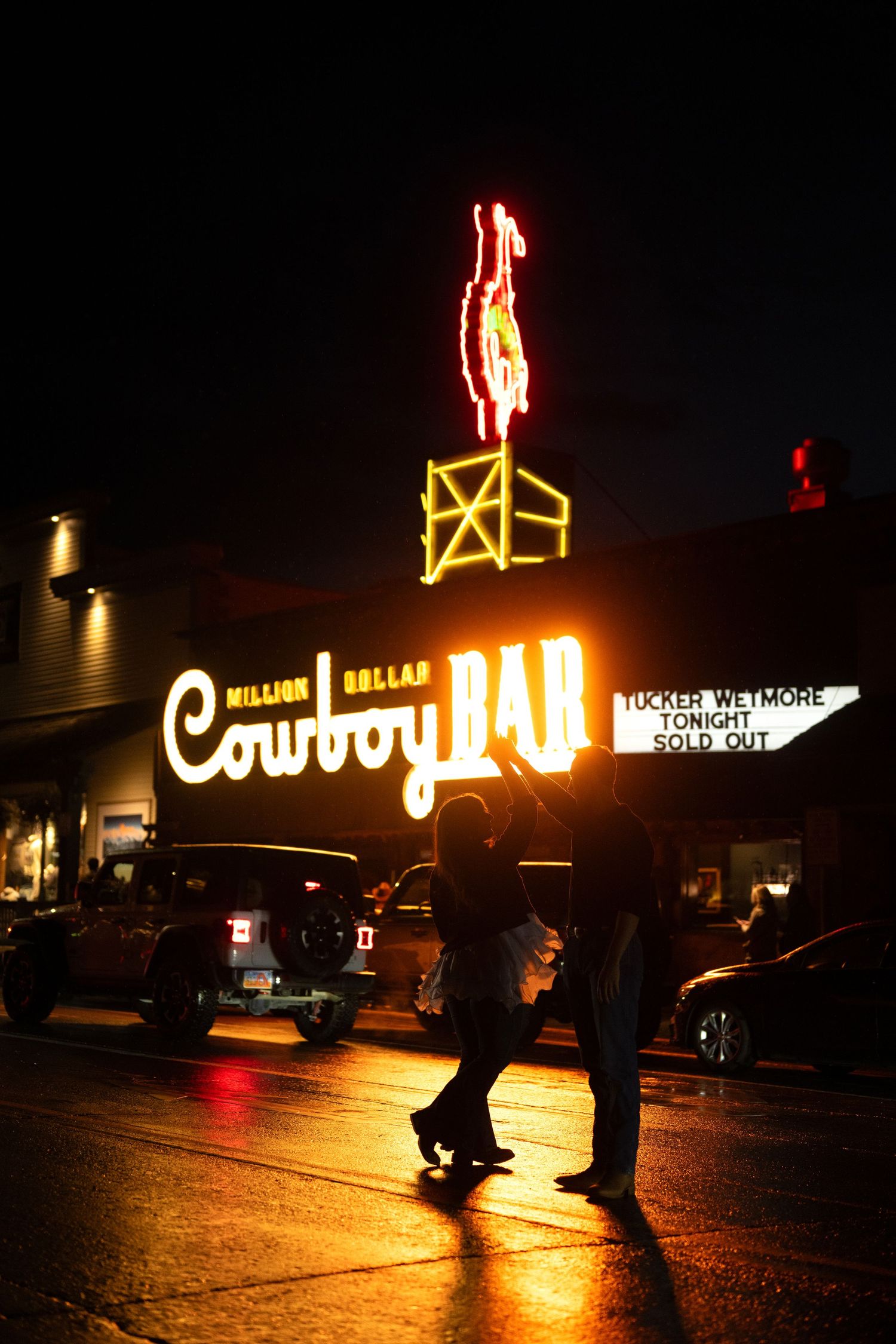 A neon sign for a cowboy bar in a nighttime urban setting.