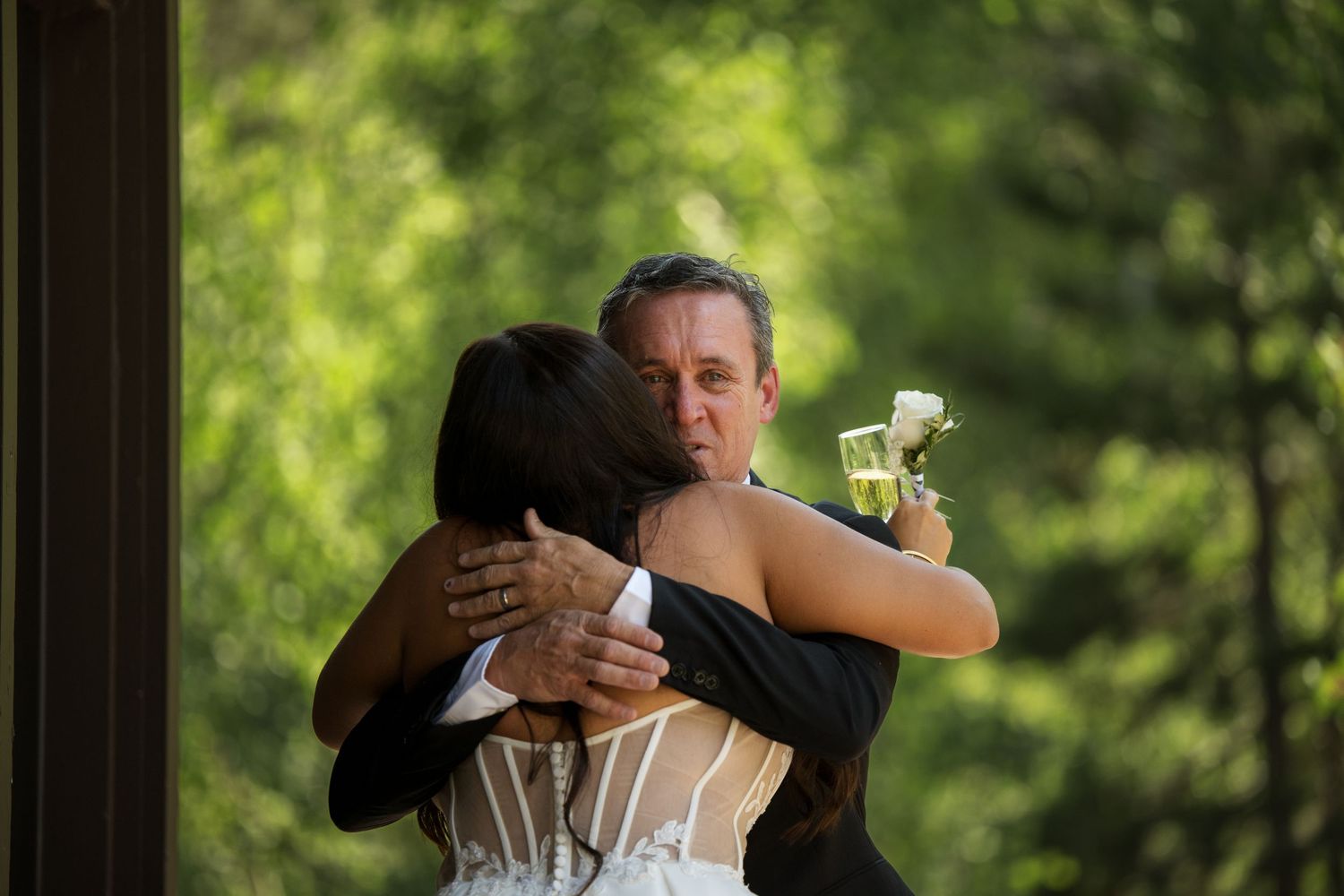 A couple embraces tenderly in a warm outdoor setting, surrounded by lush greenery.
