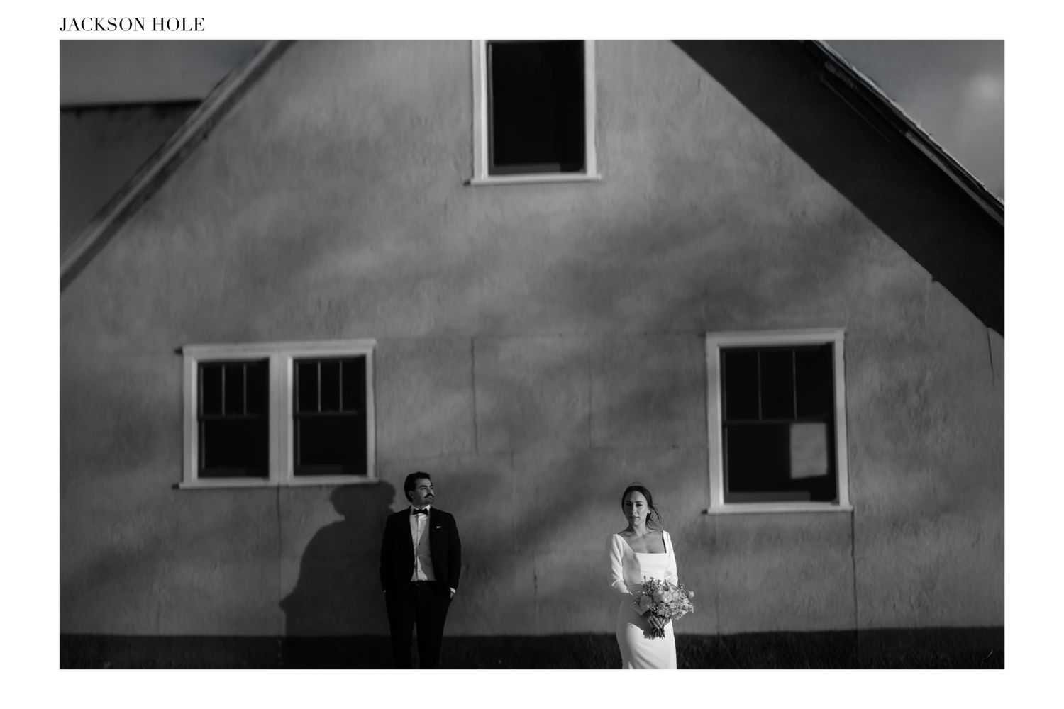 Black and white wedding photo of bride and groom standing apart against a sunlit building in Jackson Hole.