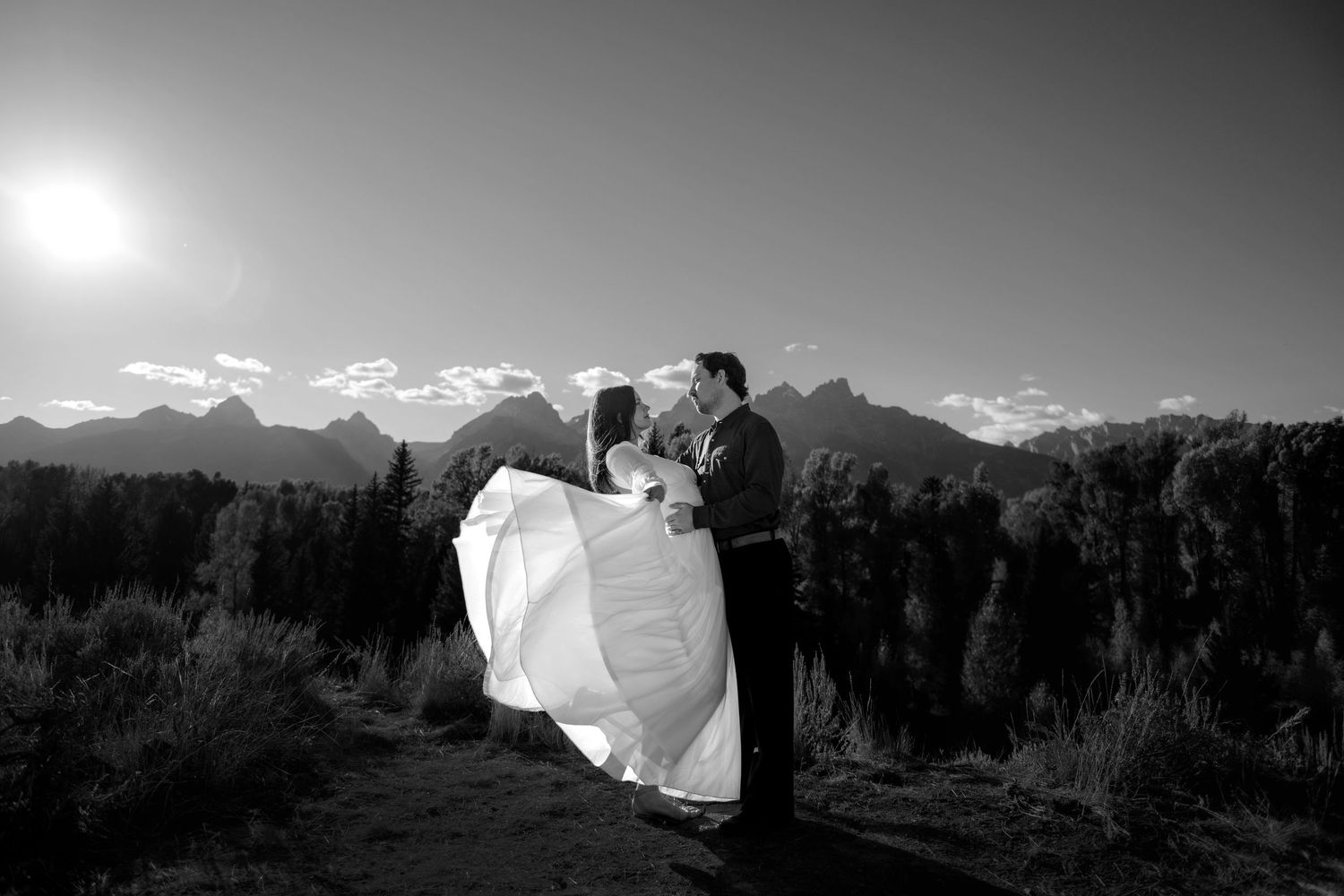 A couple embracing in a field with mountains in the background.